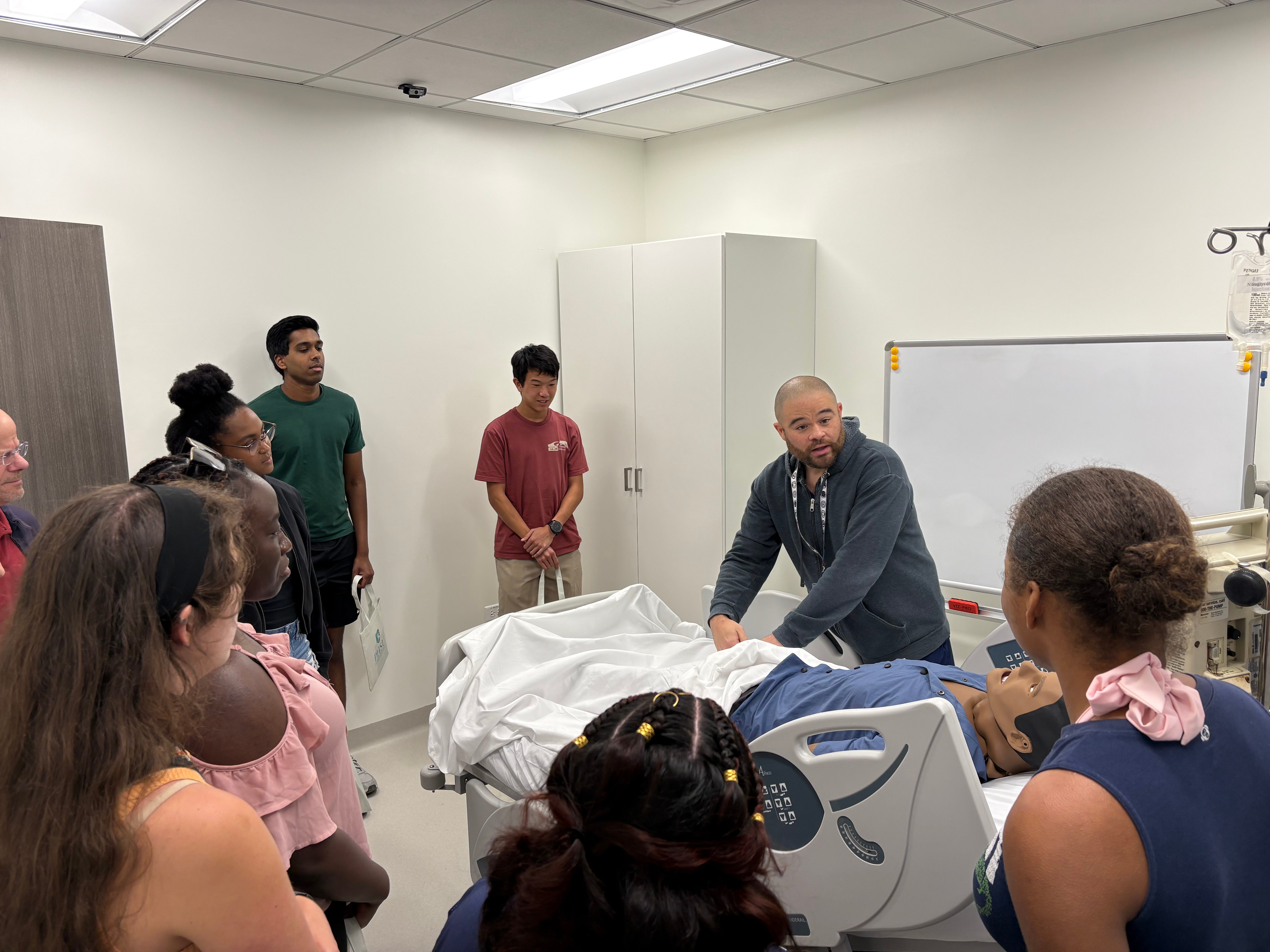 Students observe a demonstration with a dummy in a hospital bed.