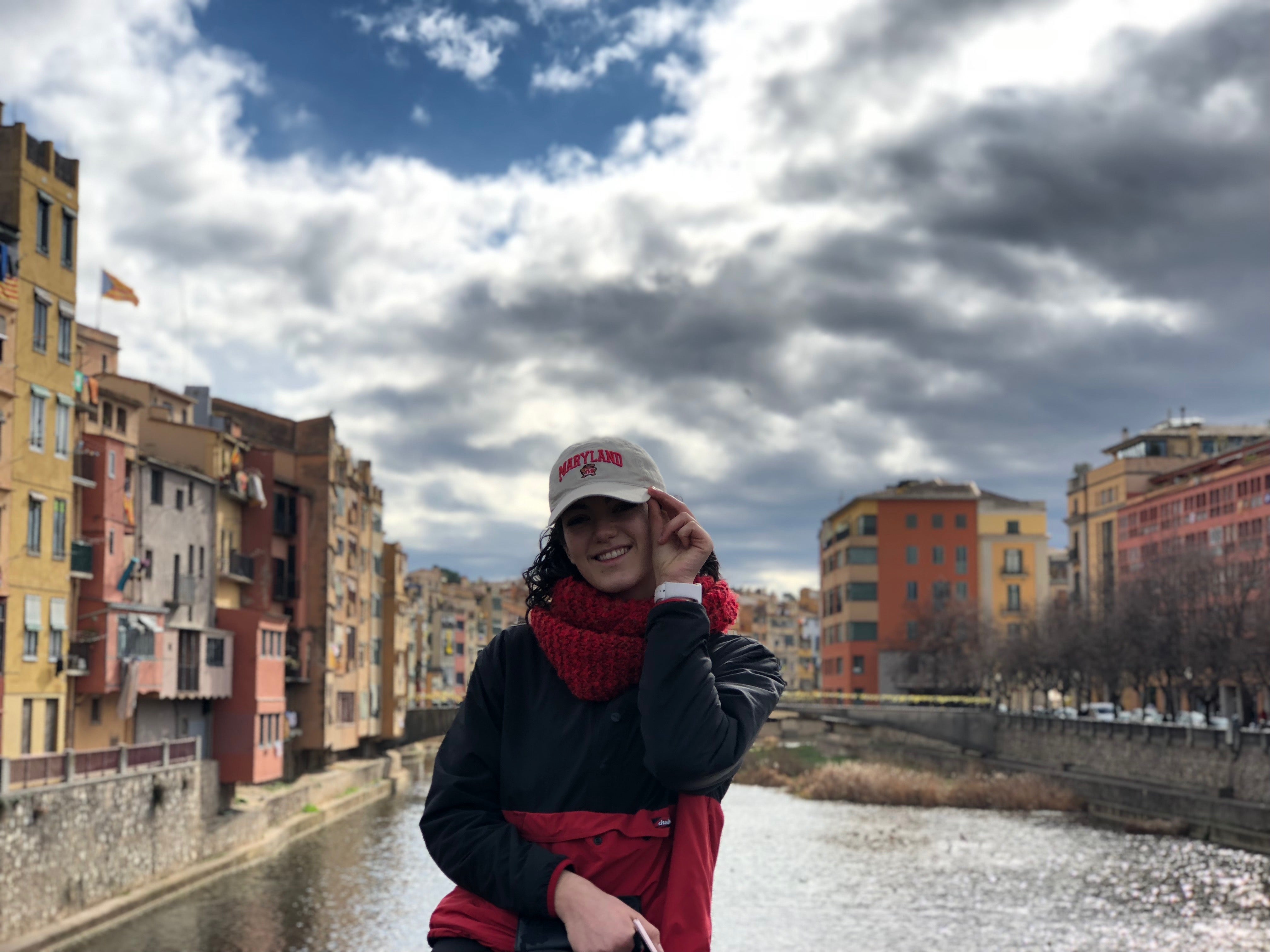 A student poses in front of a canal in Europe. She proudly wears a Maryland baseball cap.