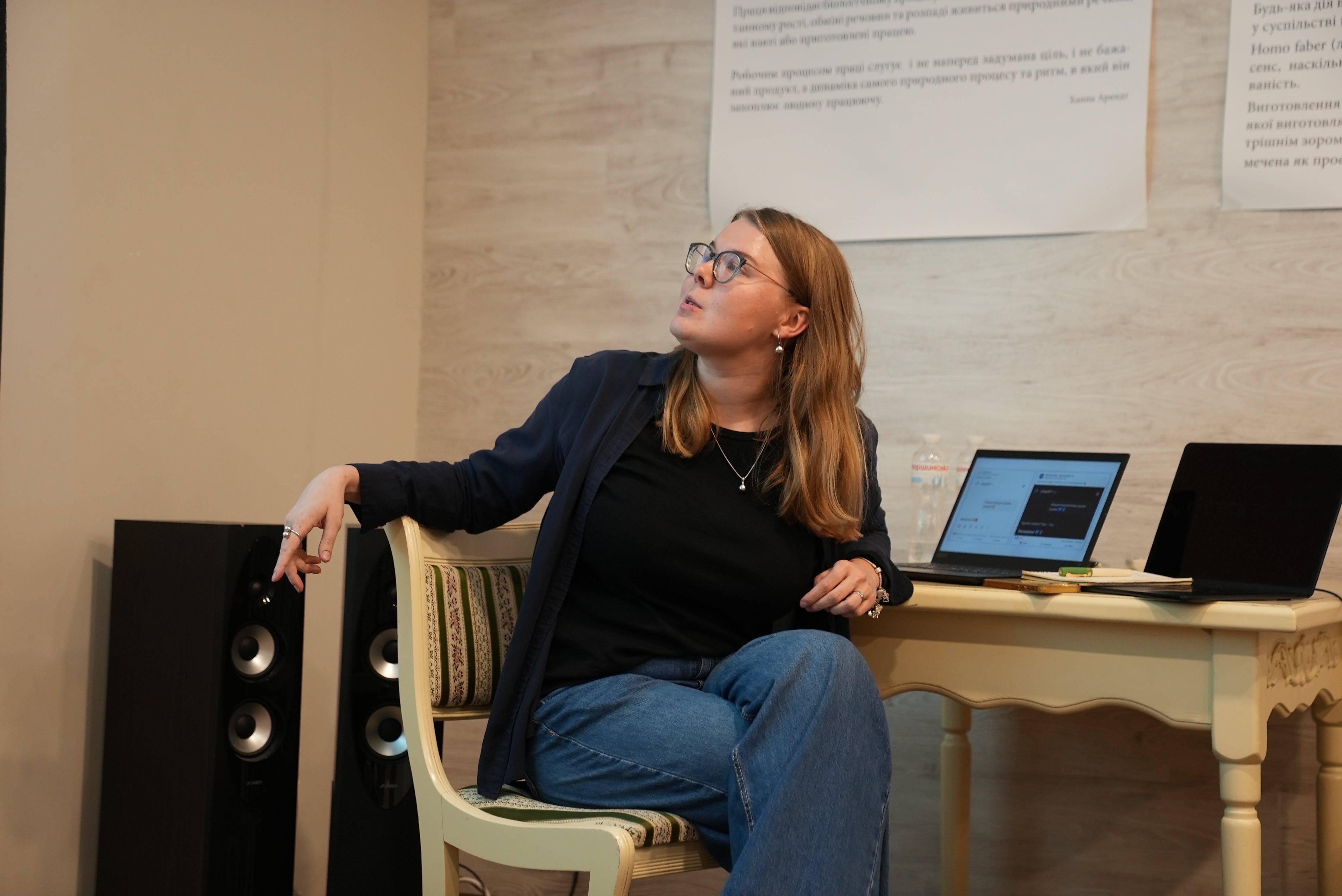 Viktoriia, a young woman, delivers a lecture, seated at a laptop, looking up at a slide out of frame