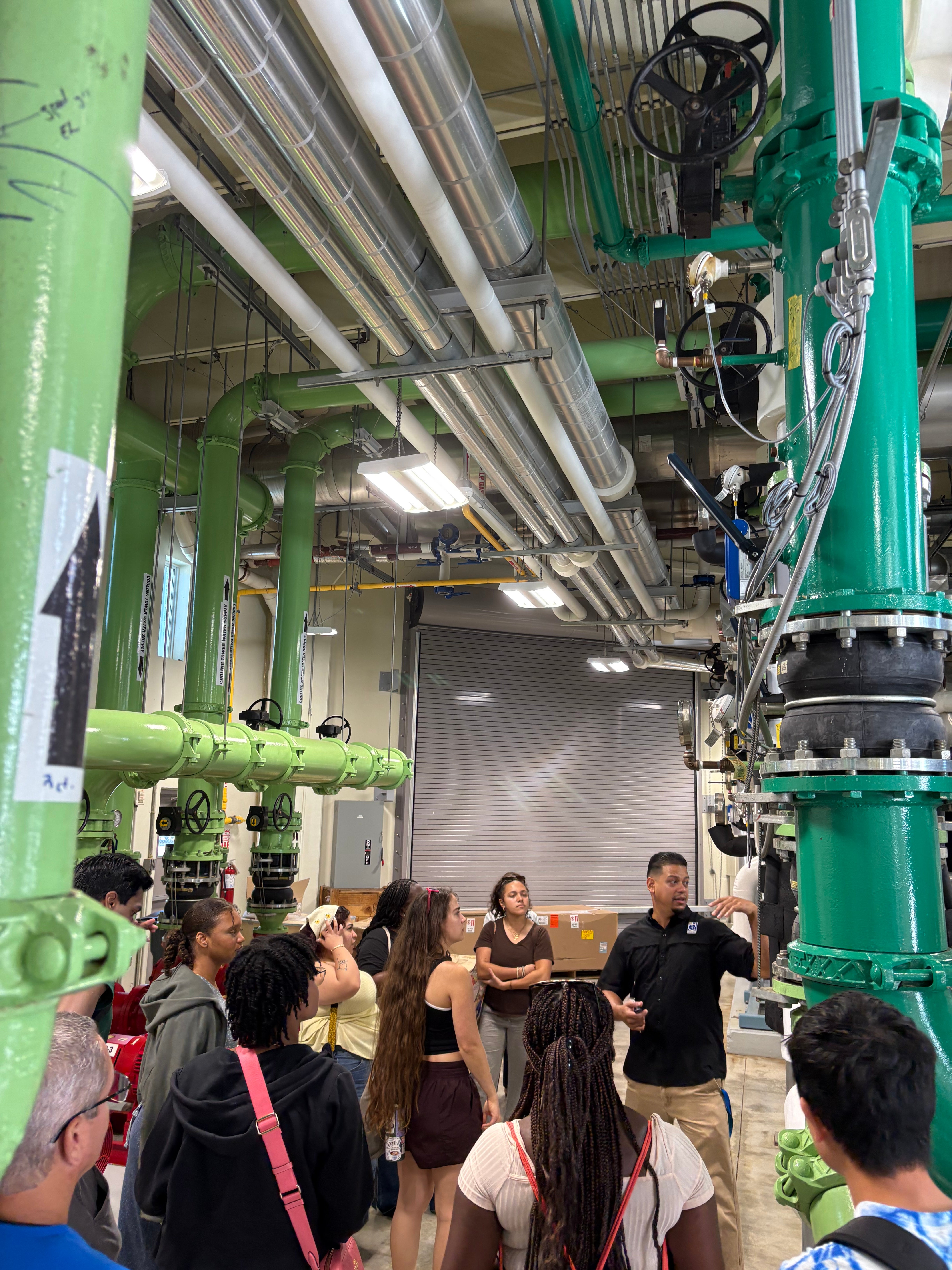 Students tour an industrial setting with large green pipes