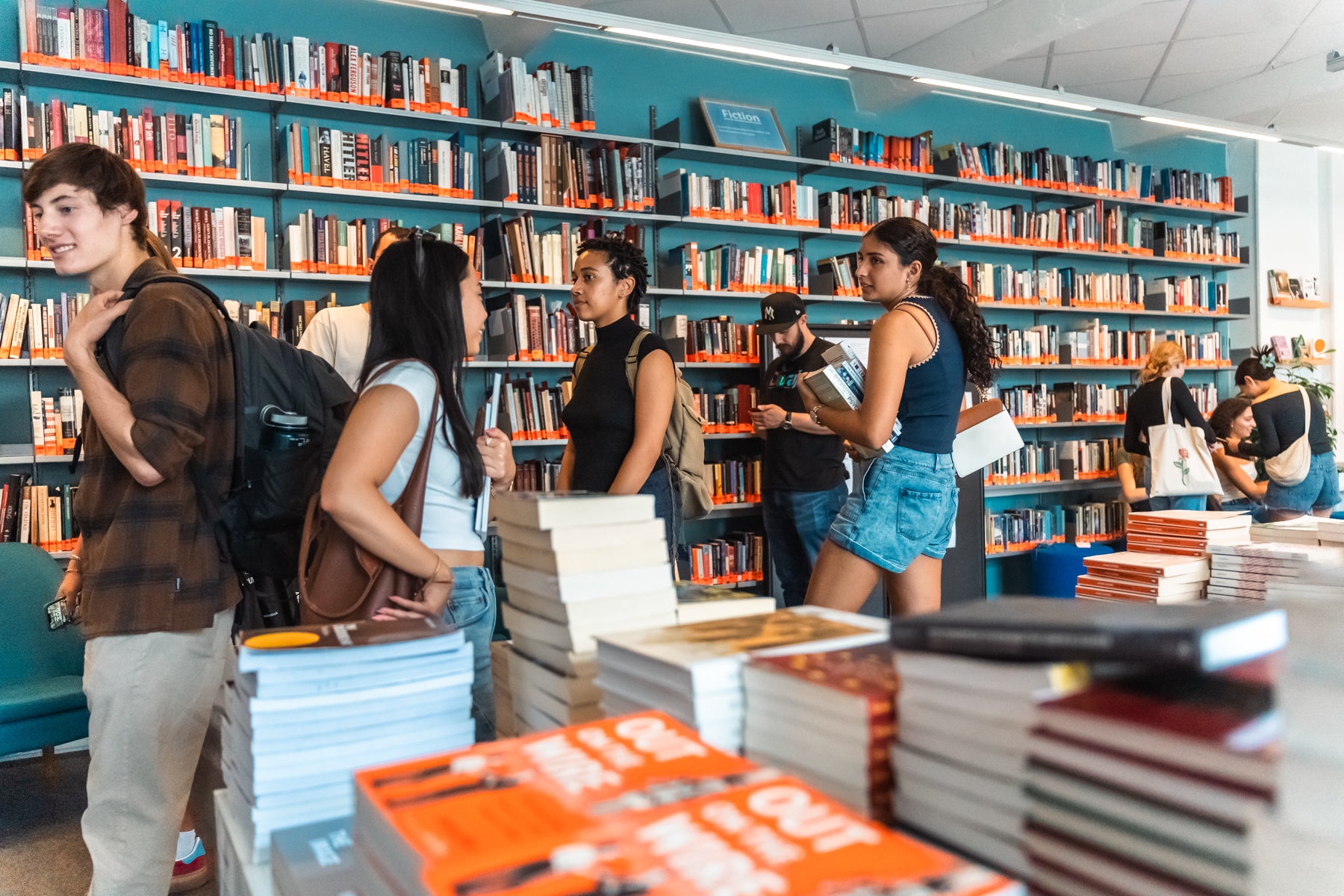 Students browse books and chat inside a bookstore with tall shelves filled with colorful titles.