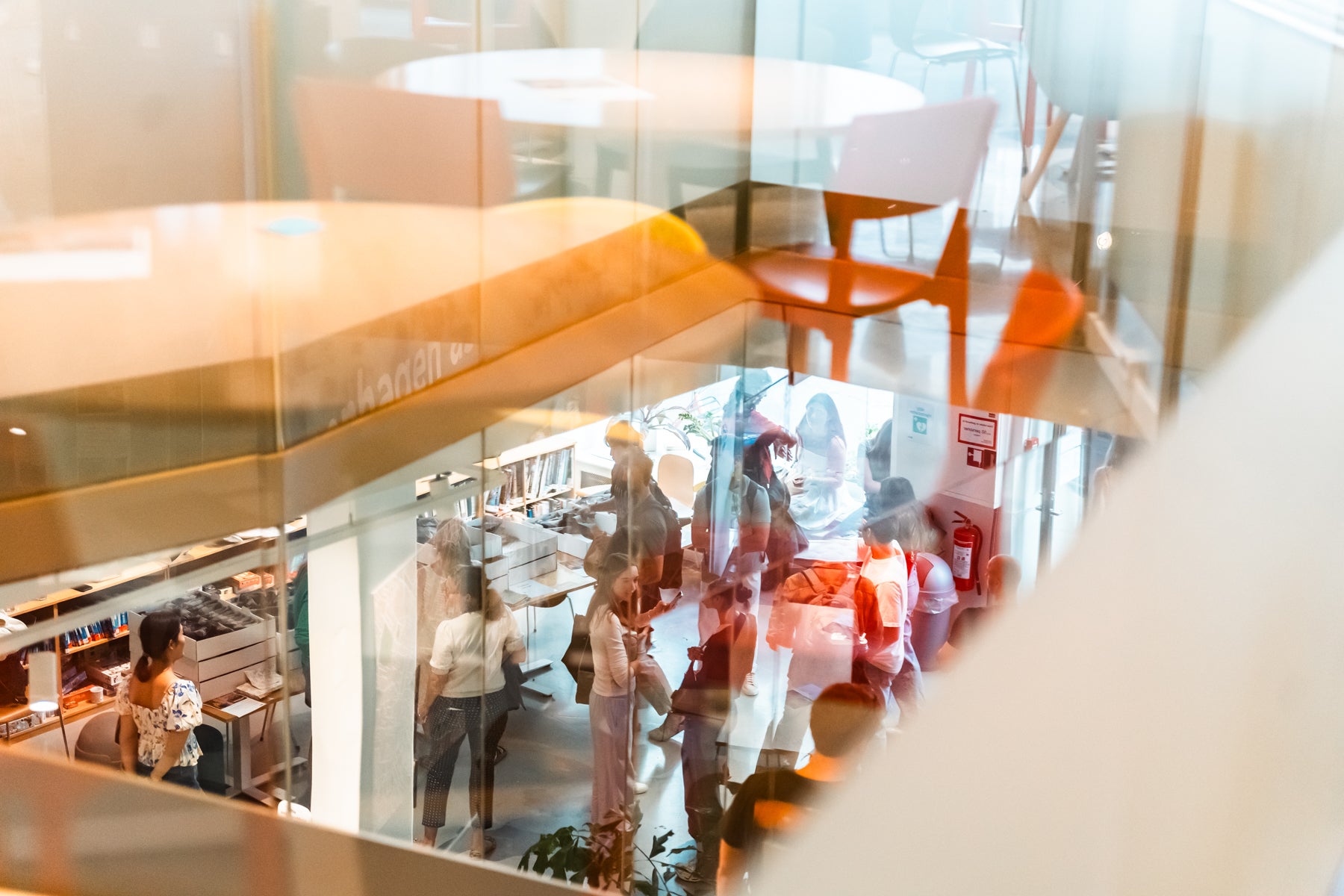 Students gather and talk in a bright, modern indoor space viewed through glass reflections.