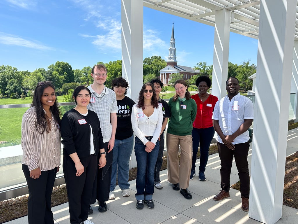 Nine individuals gather on a rooftop with the UMD Chapel in the background