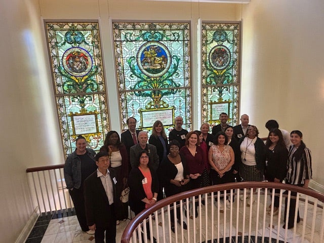 Group photo of HREx symposium participants in front of stained glass windows at the MD General Assembly