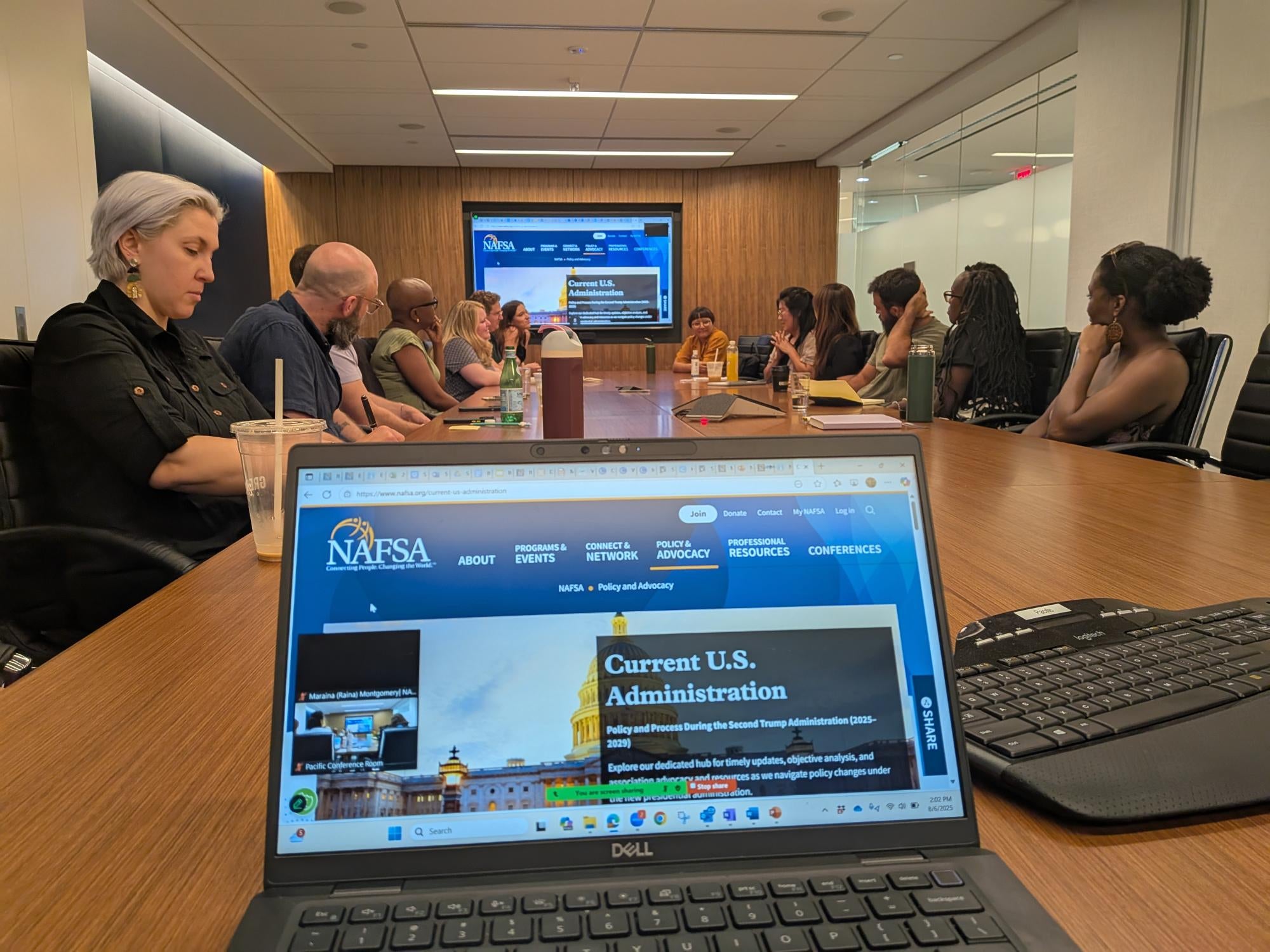 Laptop displaying NAFSA website with a conference table full of EA staff in the background