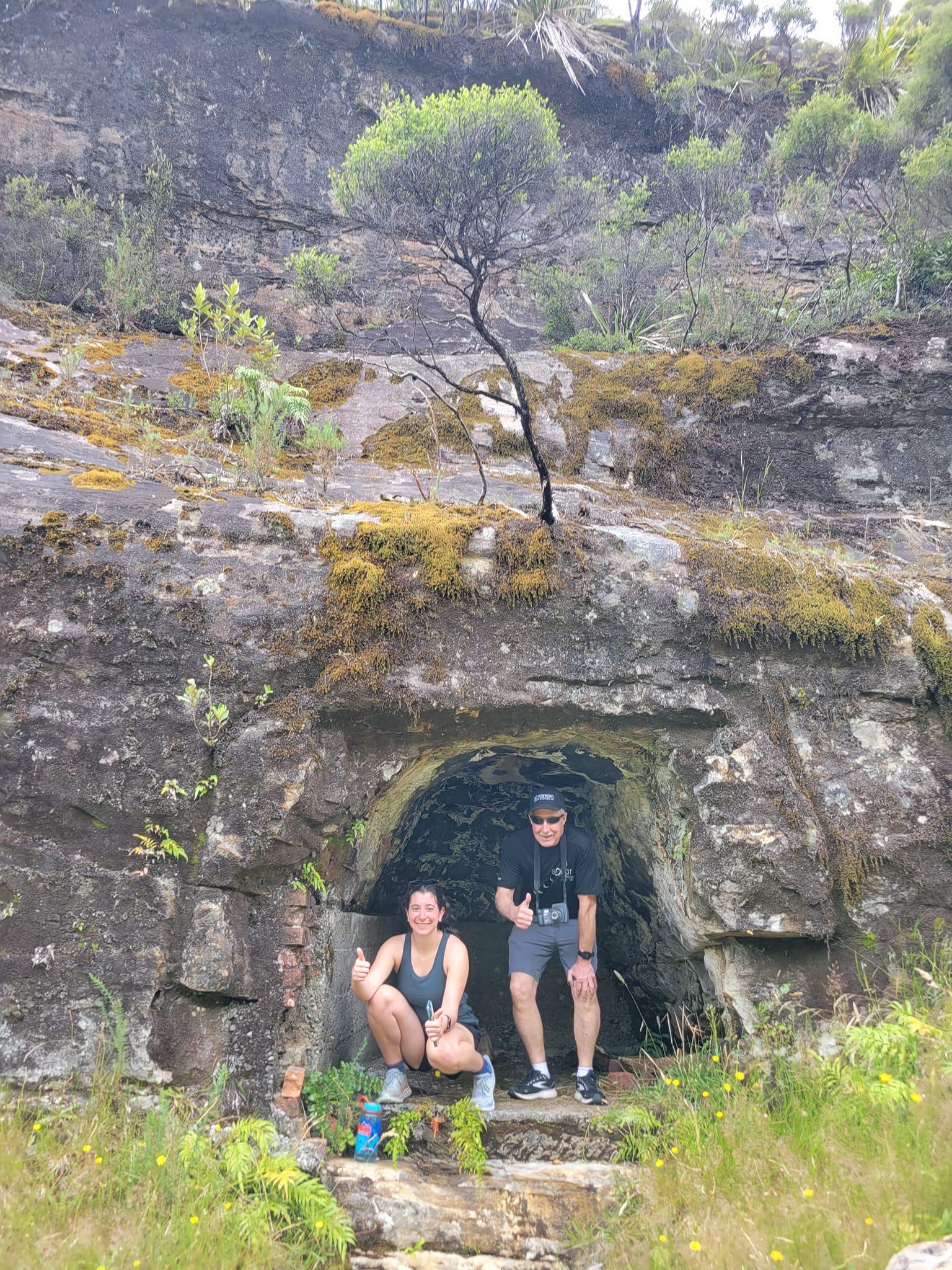 A man and a woman crouch in a rock alcove.