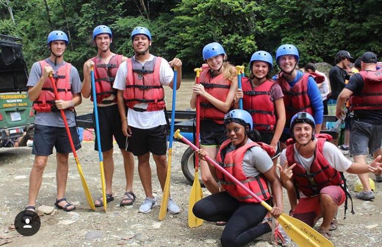UMD student, Grace Okpali, poses with other USAC Costa Rica students before a white water rafting trip. They wear life jackets and hold paddles. 