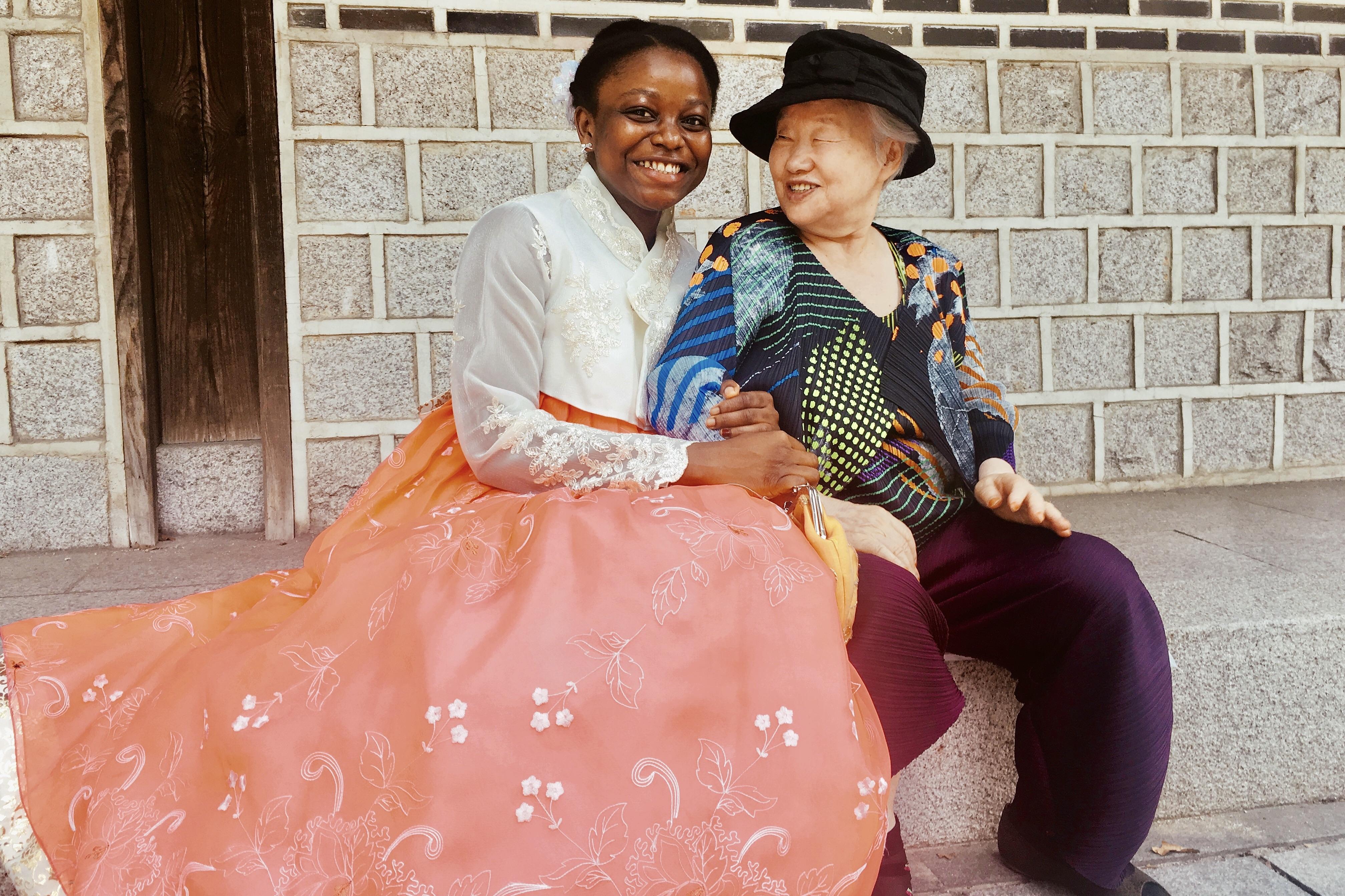 Student in a traditional hanbok sits and holds the arm of a smiling older Korean woman.