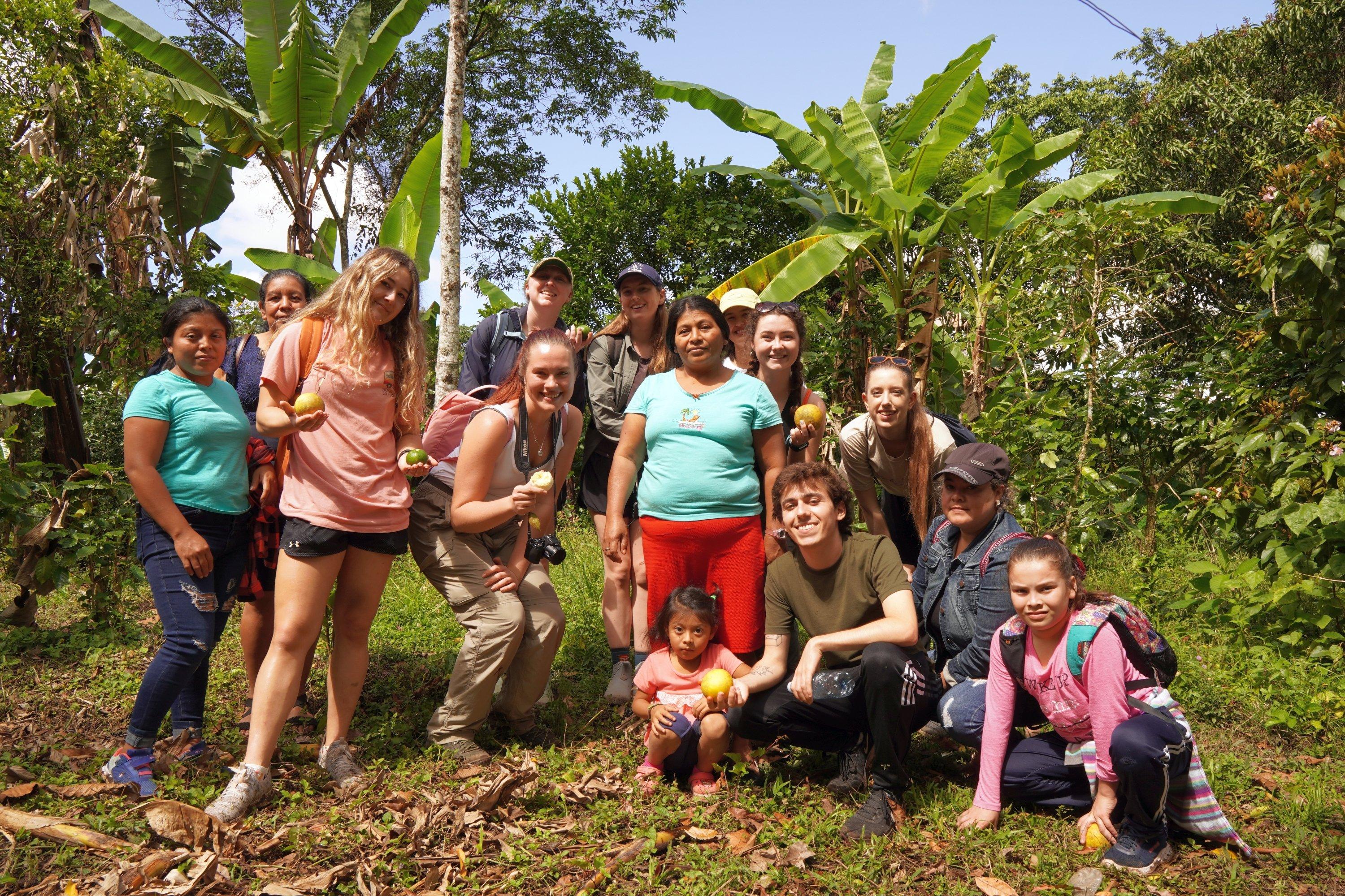 Students standing and kneeling, holding fruit alongside local residents on their study abroad program. 