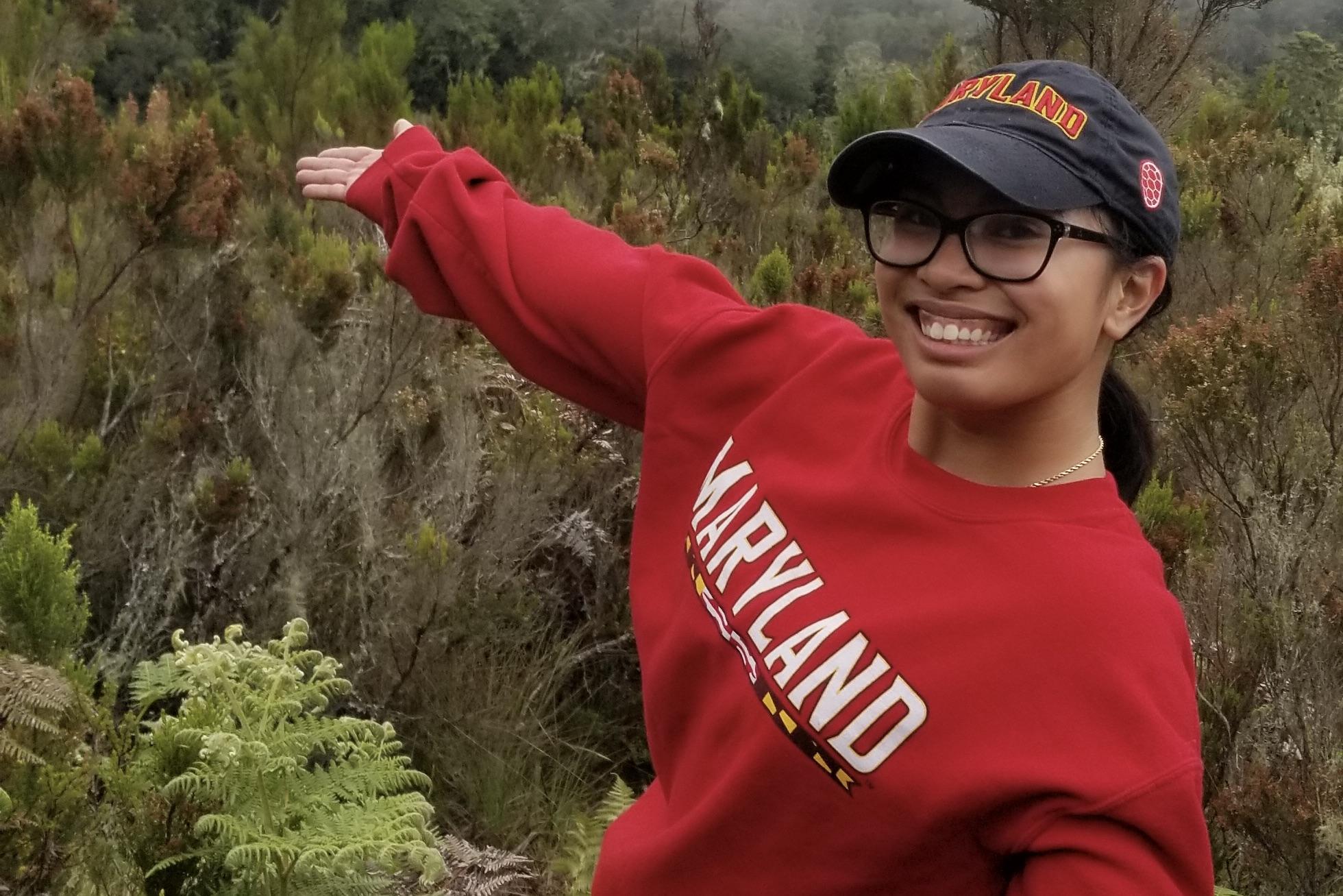 UMD student in Tanzania smiles from the top of a mountain. She wears a Maryland sweatshirt and baseball cap. 
