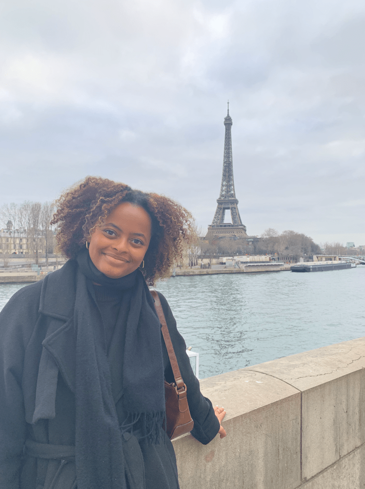 Sophia Wooden poses at the Seine river in Paris. The Eiffel Tower can be seen on the other side of the riverbank.