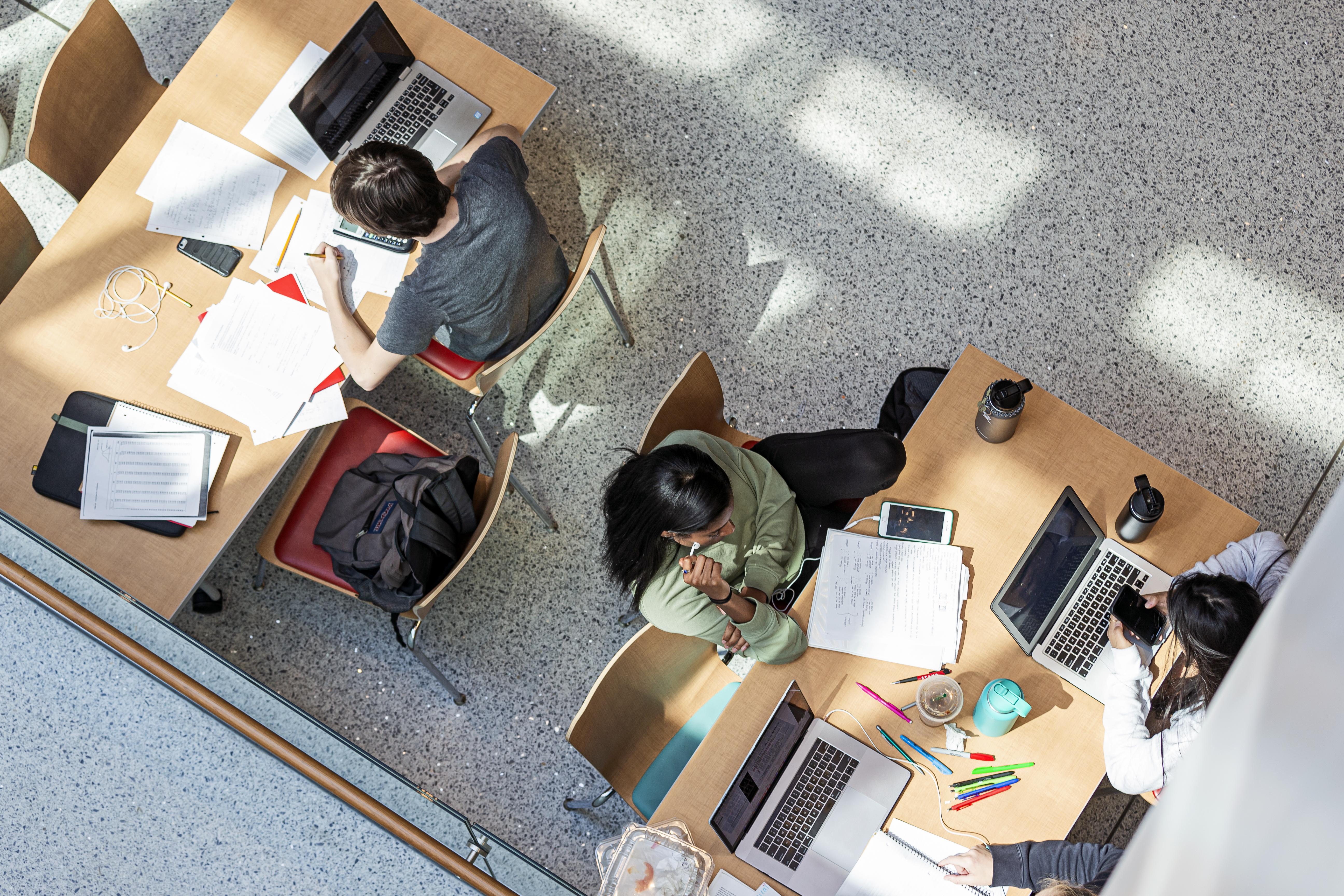 Overhead view of students sitting at tables on their laptops.