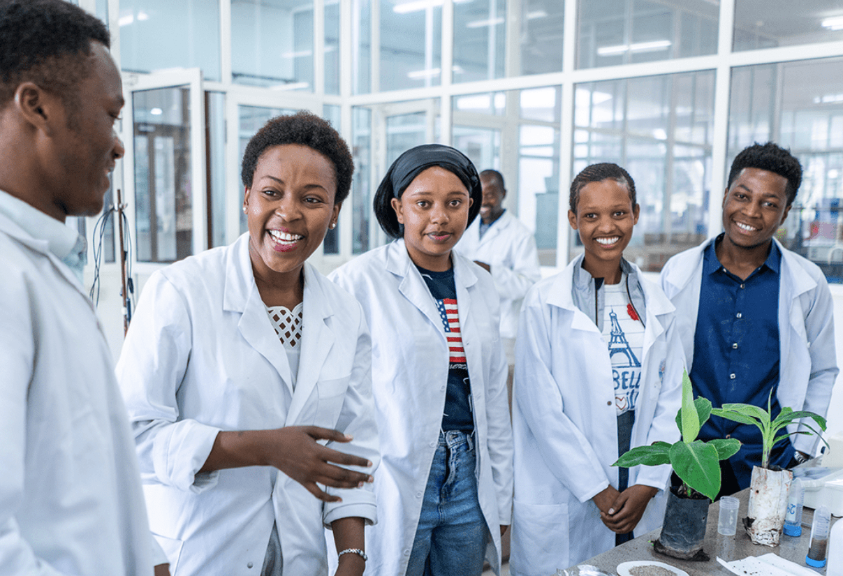 Five students in lab coats stand at a lab station with plants