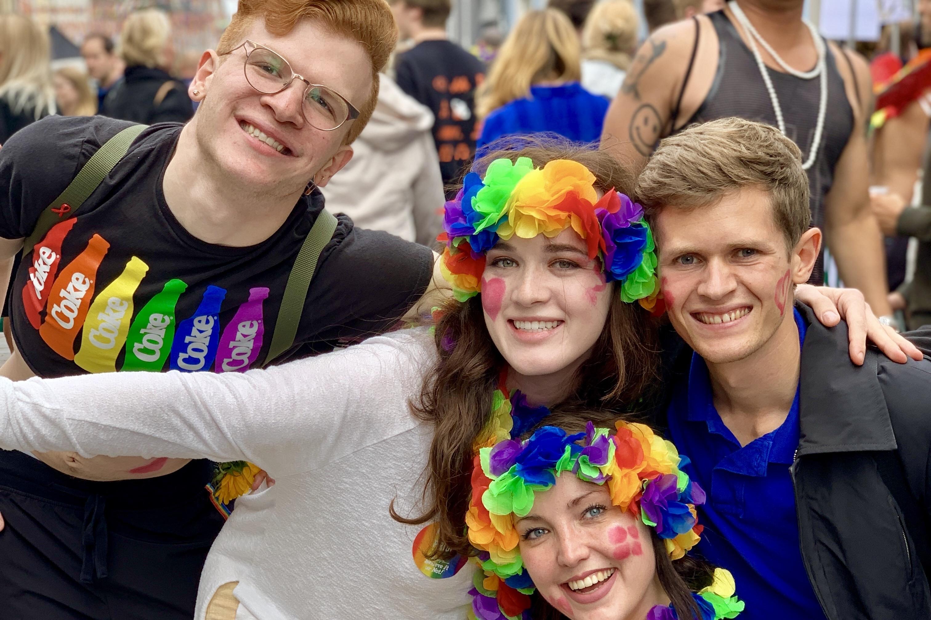 Four students celebrating a the Copenhagen Pride Parade. They wear rainbow leis and clothes.