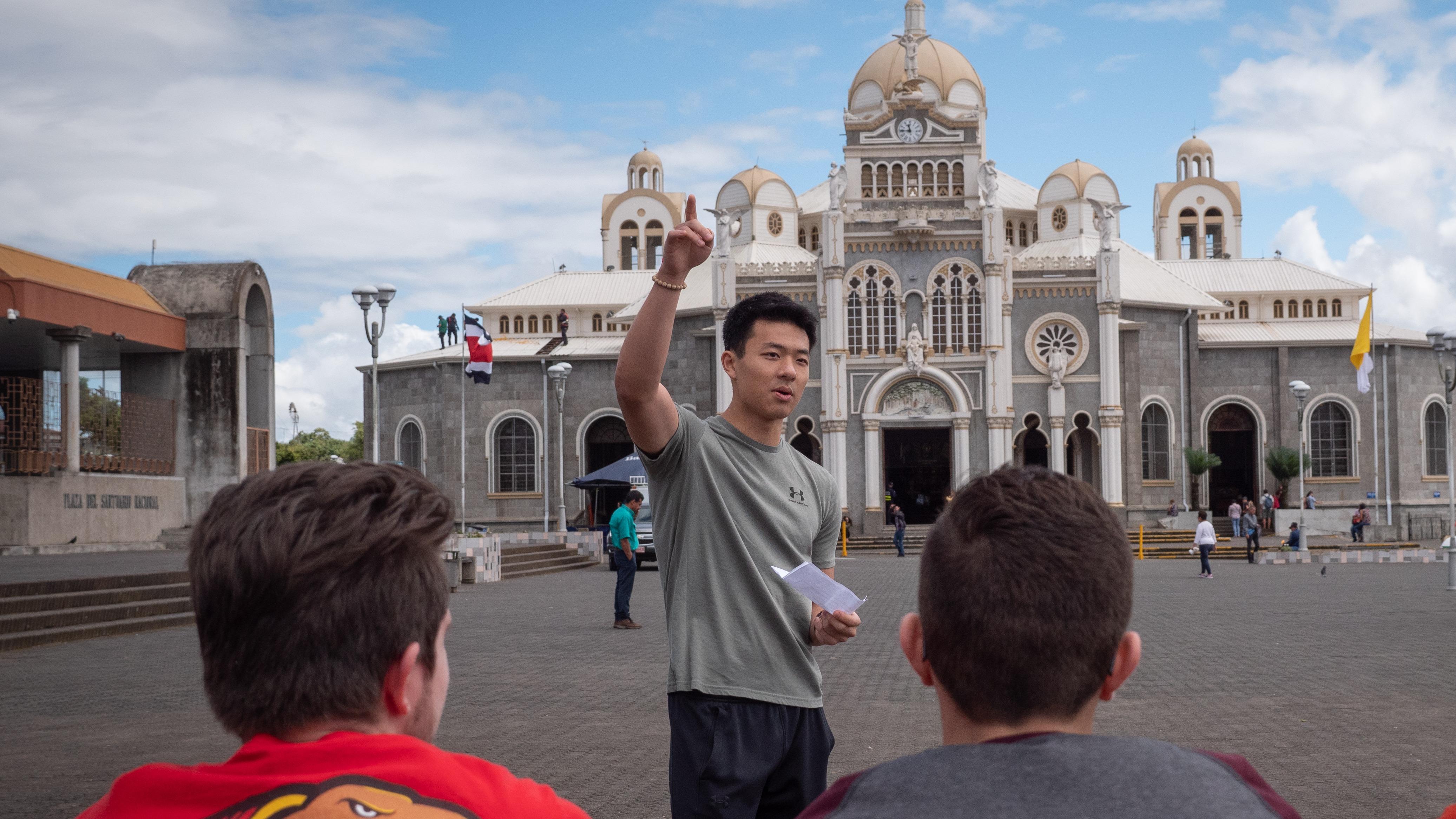 Study abroad student stands in front of a church in Costa Rica talking to other students.