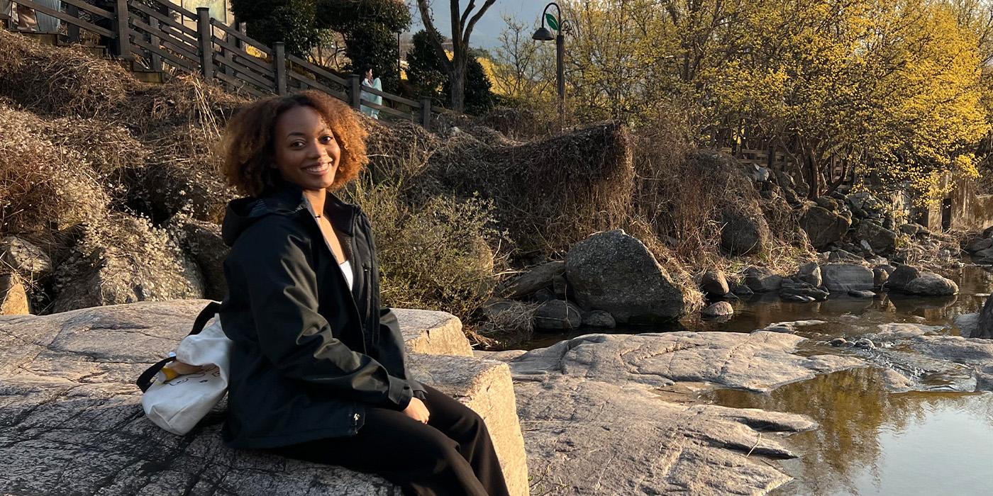 Alyssa Taylor in a black rain jacket sitting by a lake in South Korea