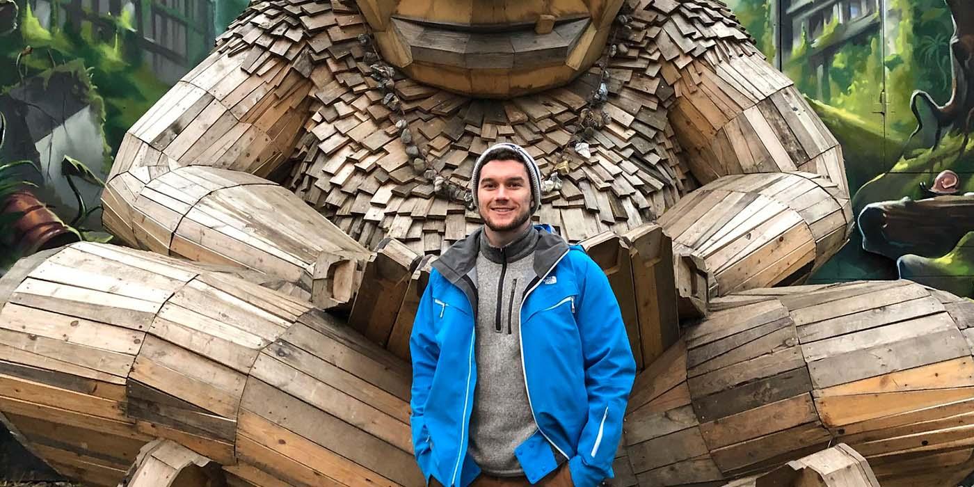 Braden House in a blue jacket, standing in front of a large wooden man in Denmark