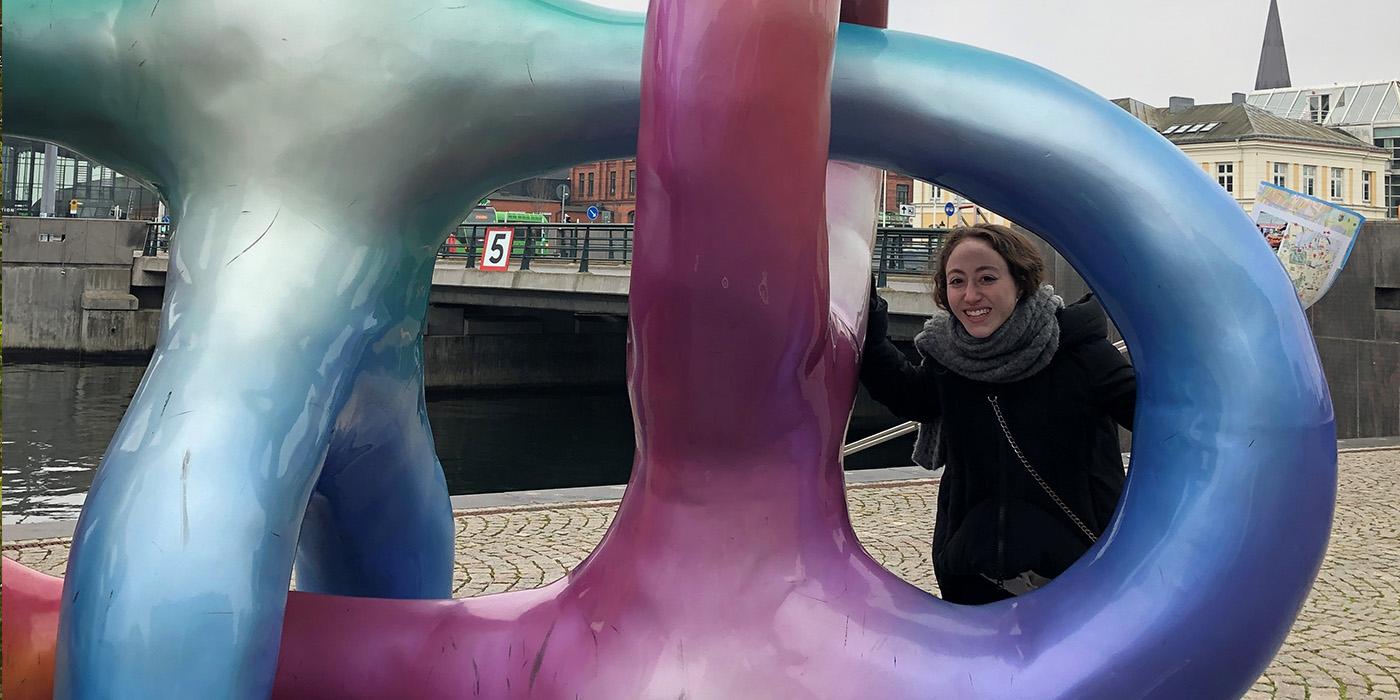 Carli Fine poses beside a large  multicolored sculpture