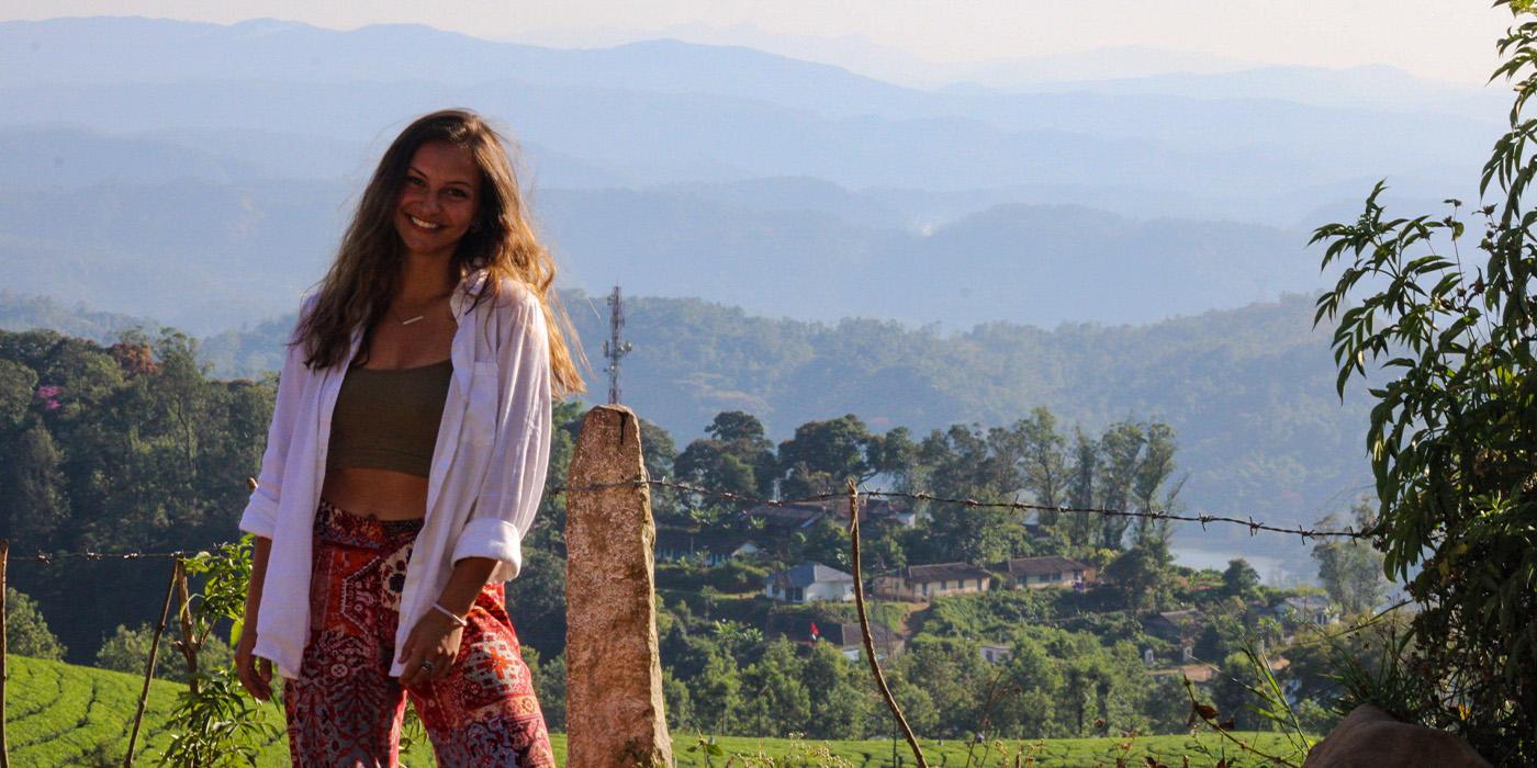 Faith Ensor smiles in front of an old wire fence with forest and mountains in the distance