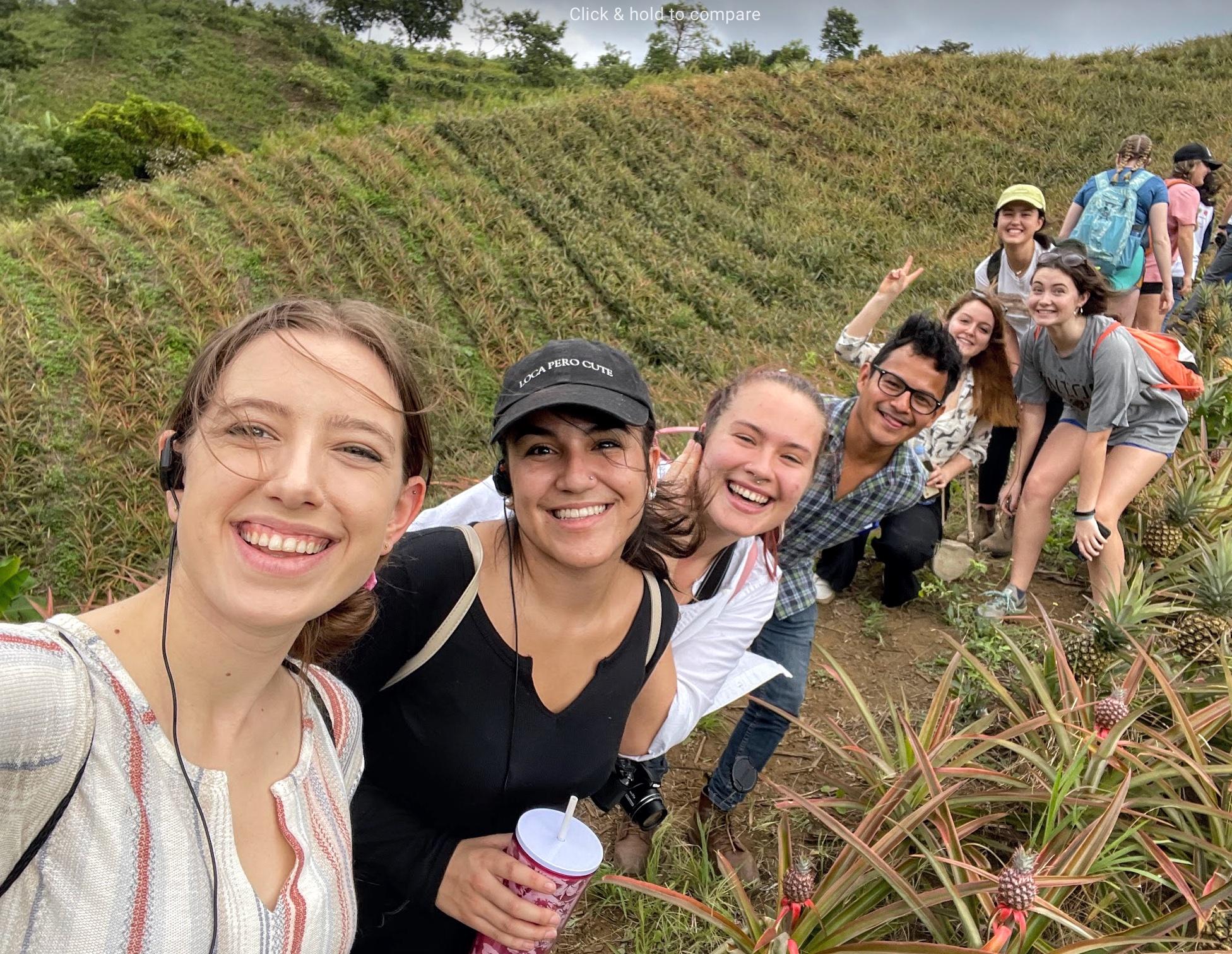 A group of seven UMD students walking down an path in a field pause for a selfie.