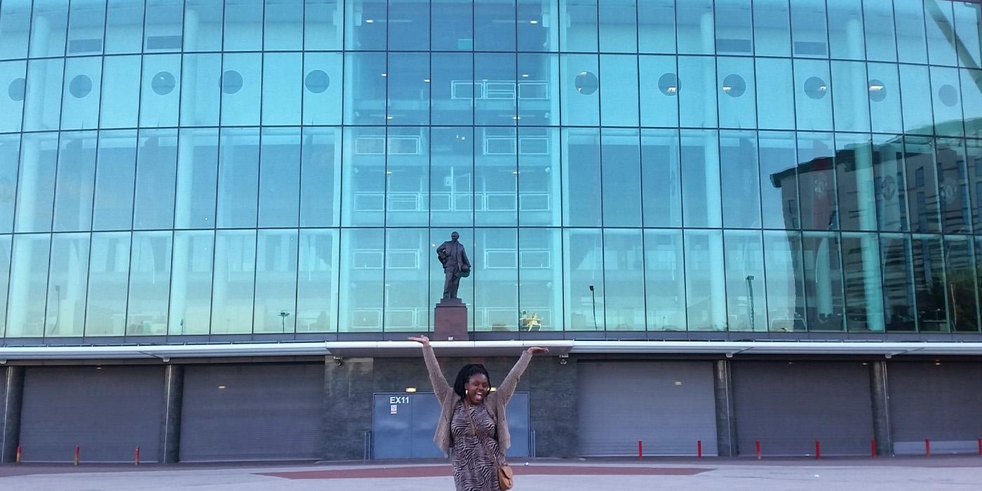 Gessica Fleurival outstretches her arms in front of the Manchester United Stadium in the United Kingdom