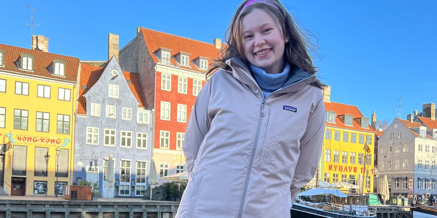 Isabel Layton wears an off white parka and smiles at a dock in Copenhagen