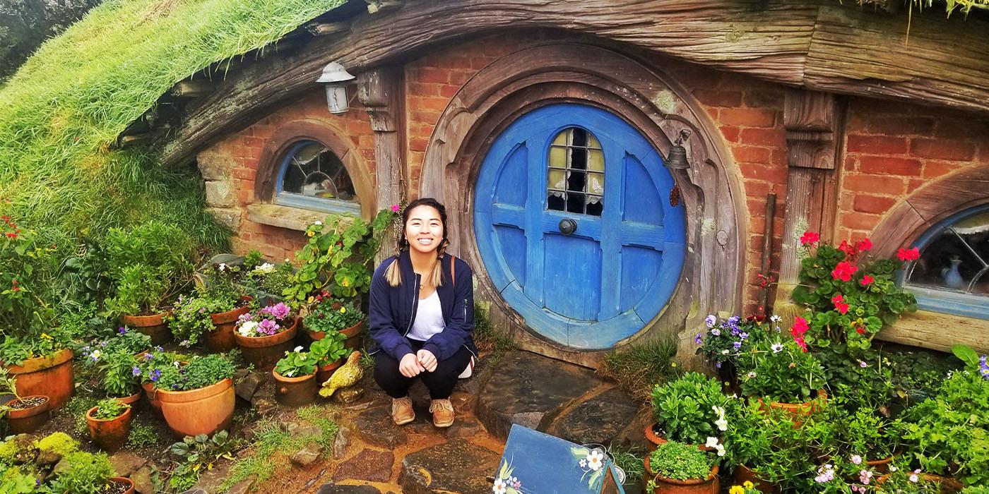 Ivy crouching in front of a circular blue door on the Hobbiton Movie Set in Auckland, New Zealand
