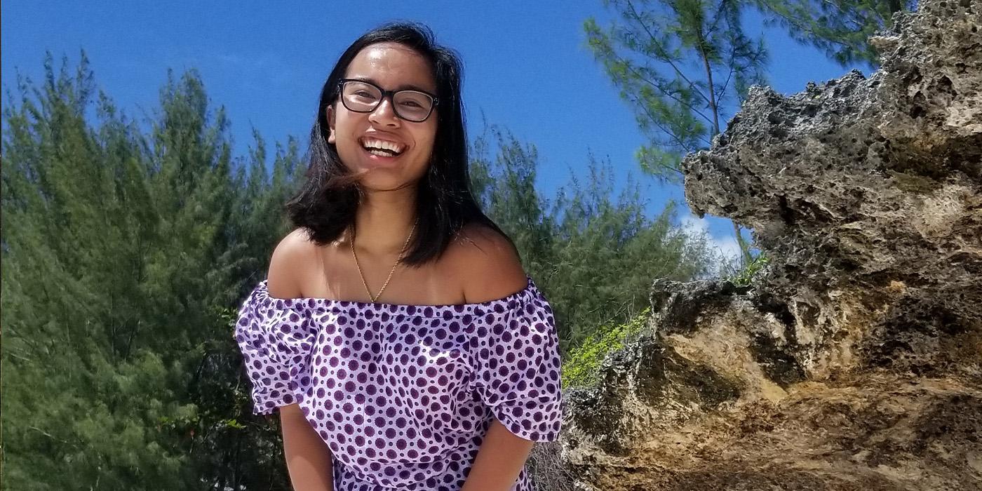 Jasmine Namata smiling and wearing a purple polka dot dress on a beach in Tanzania