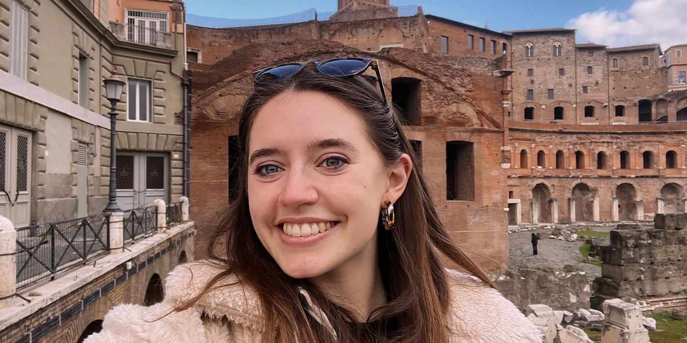 Julia Eisen wears a furry jacket and sunglasses by an Italian tourist site