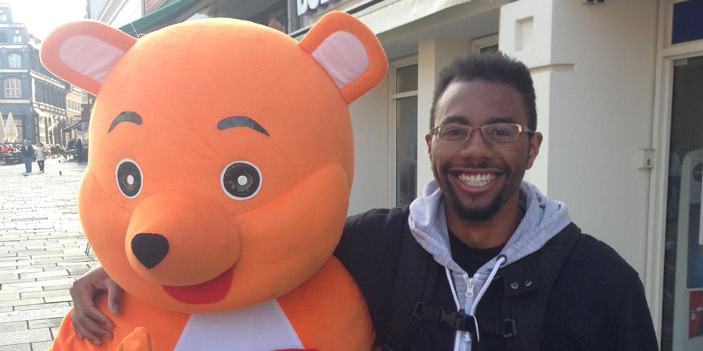 Menyae Christopher puts his arm around a person in a orange bear costume