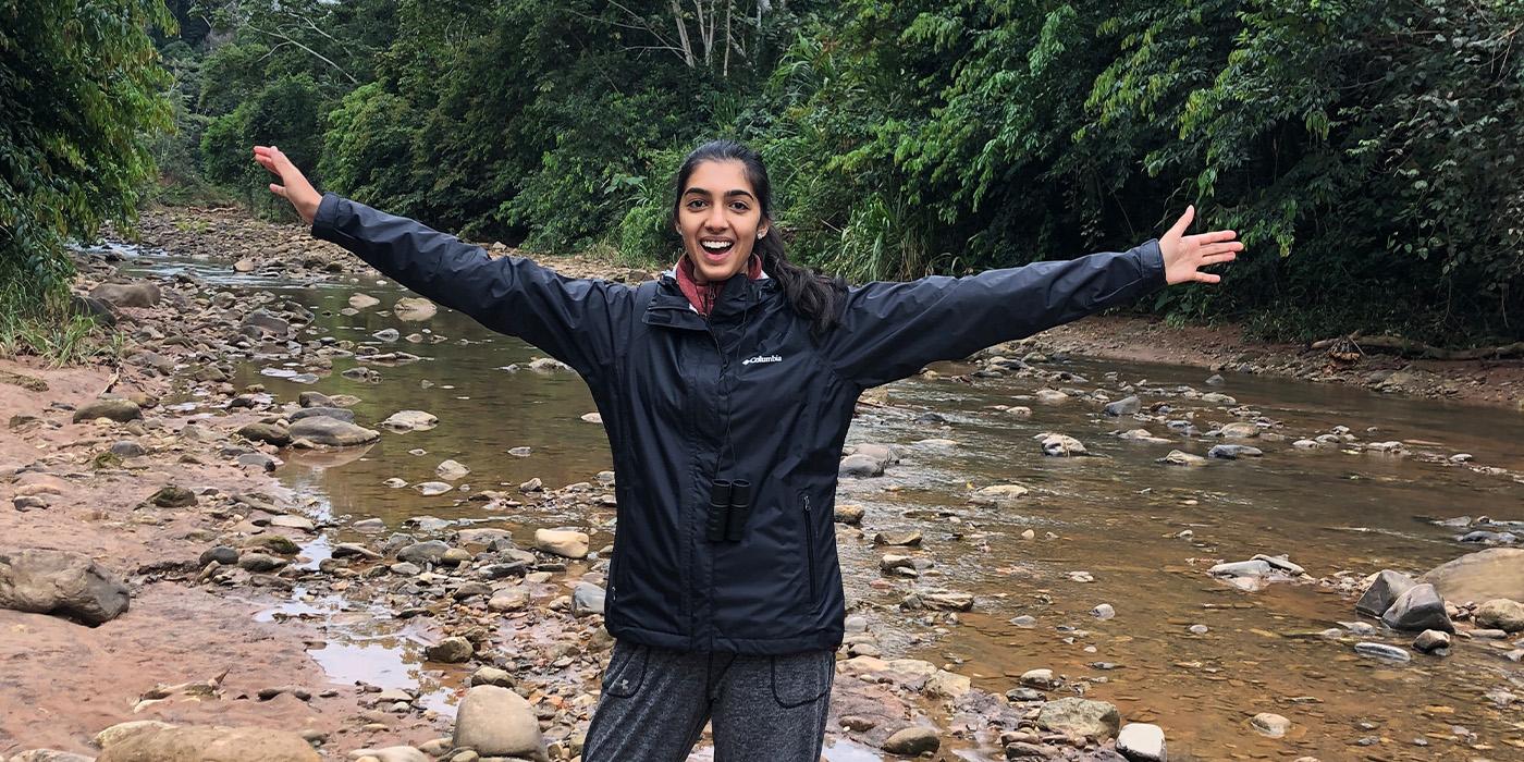 Nadia Malik outstretches her arms while smiling in a forest in Bolivia