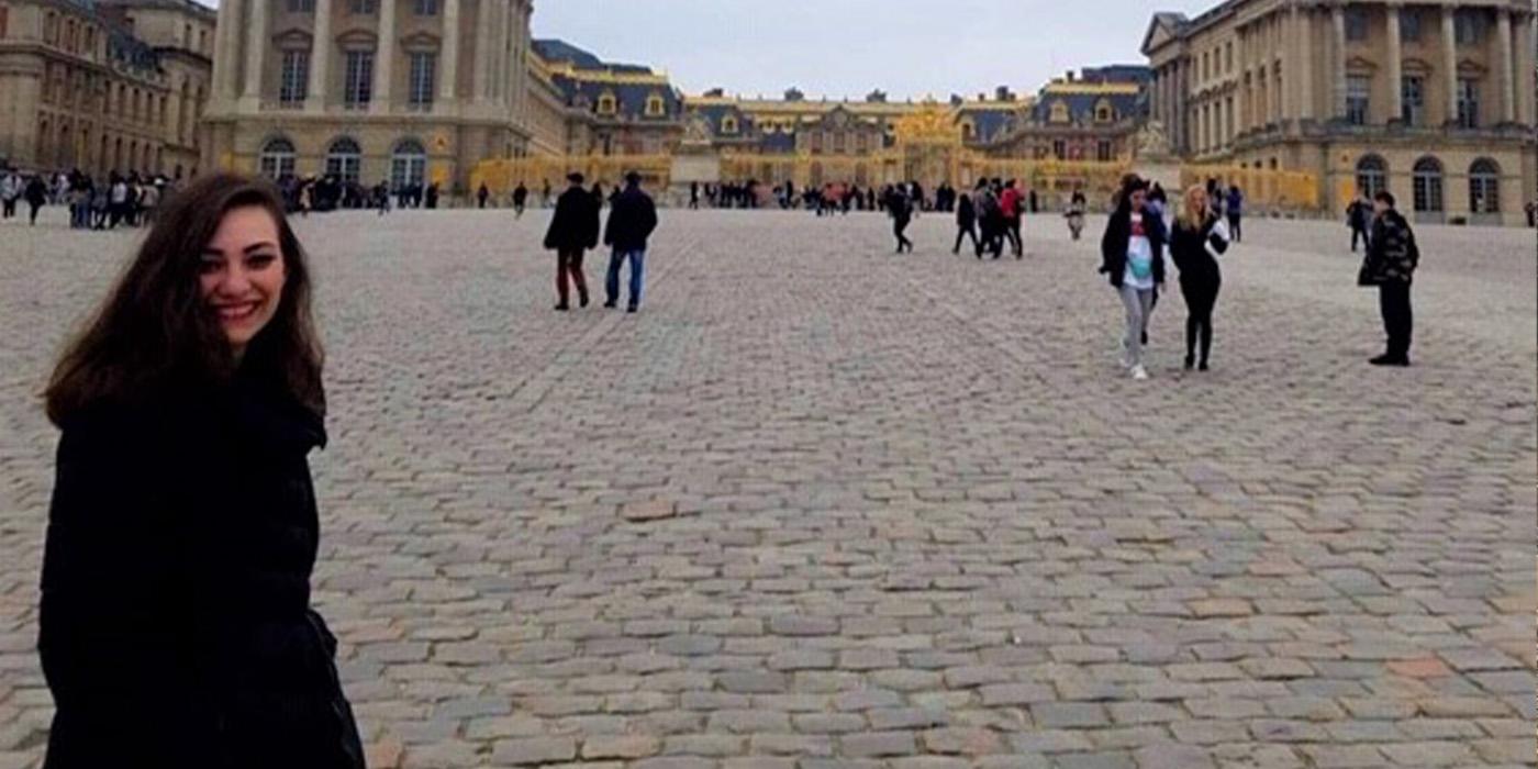 Rose Raufman, wearing a black coat, stands in front on the Palace of Versailles in France