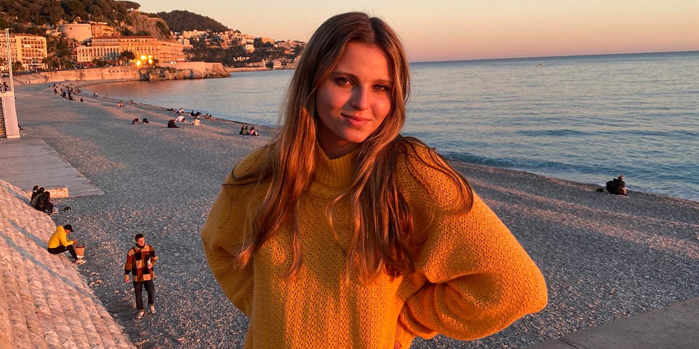 Samantha Fielder wears a mustard yellow sweater on a beach at sunset