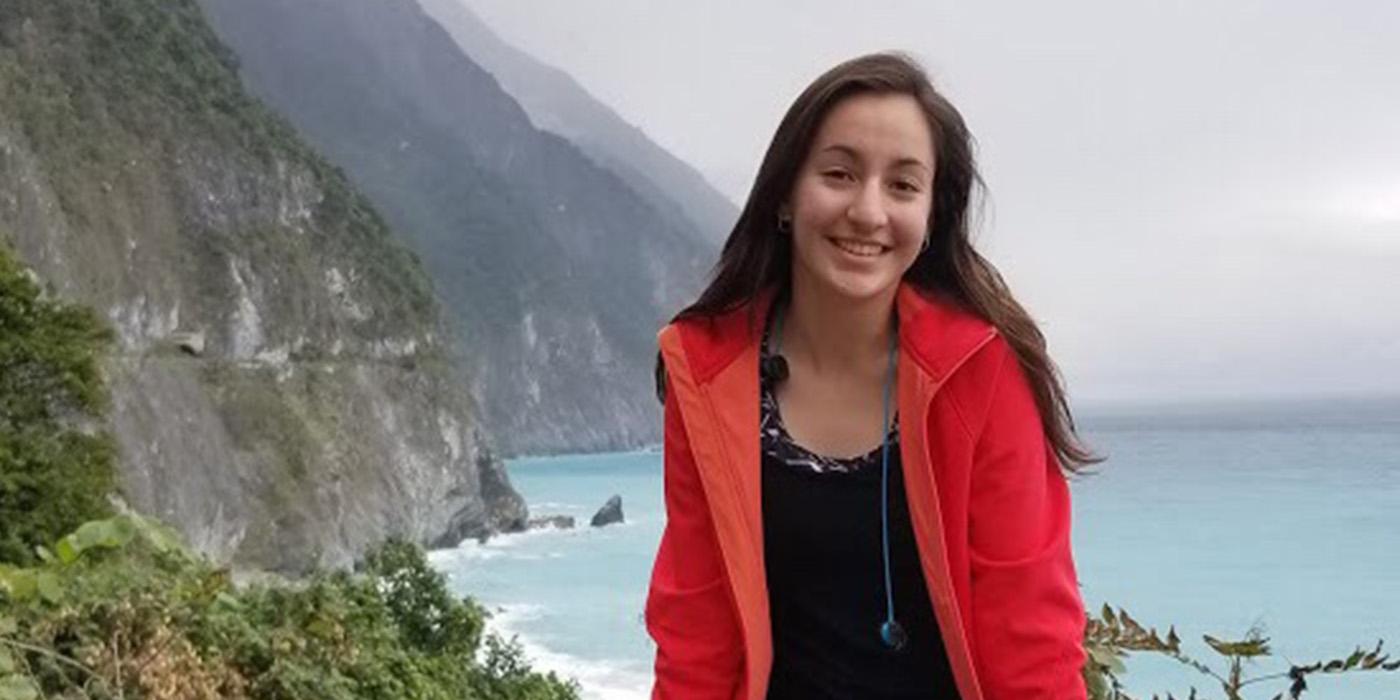 Sofia sitting on top of a railing, with mountains and a coastline behind her