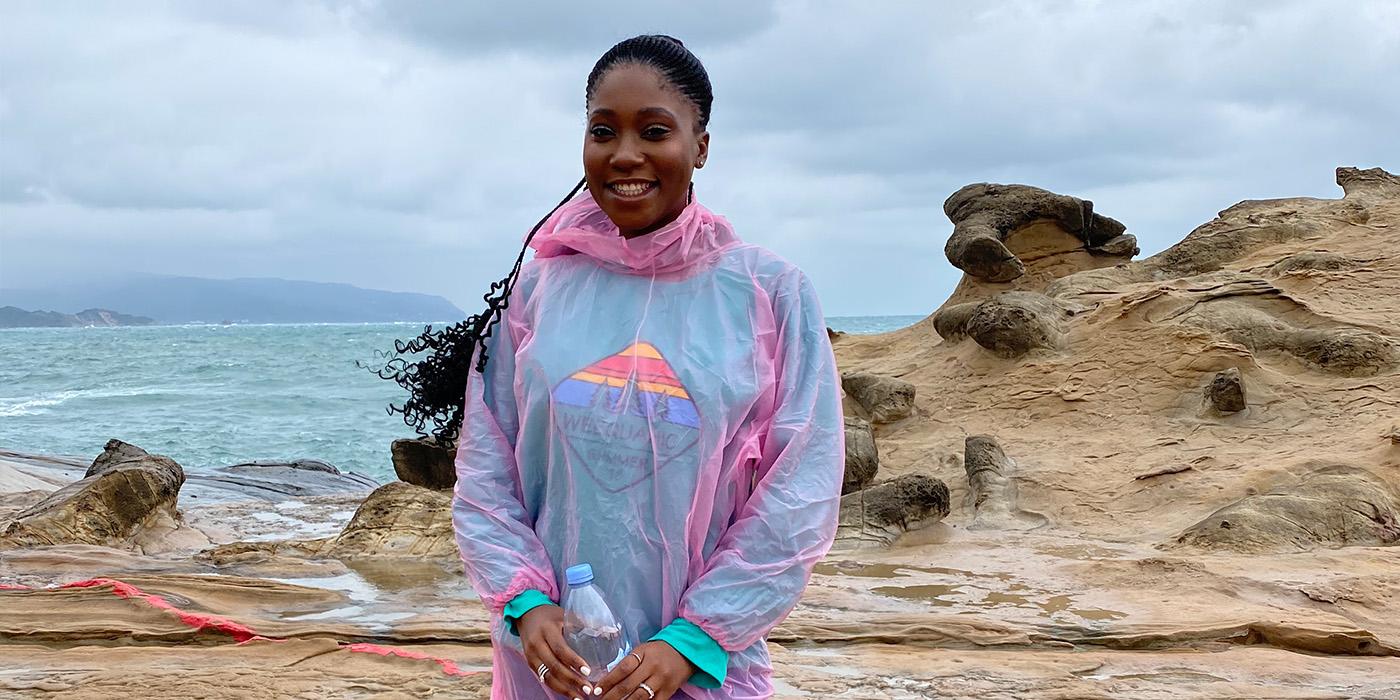 Tumi Akin-Sodipo wears a pink poncho by a rocky costal area on an overcast day