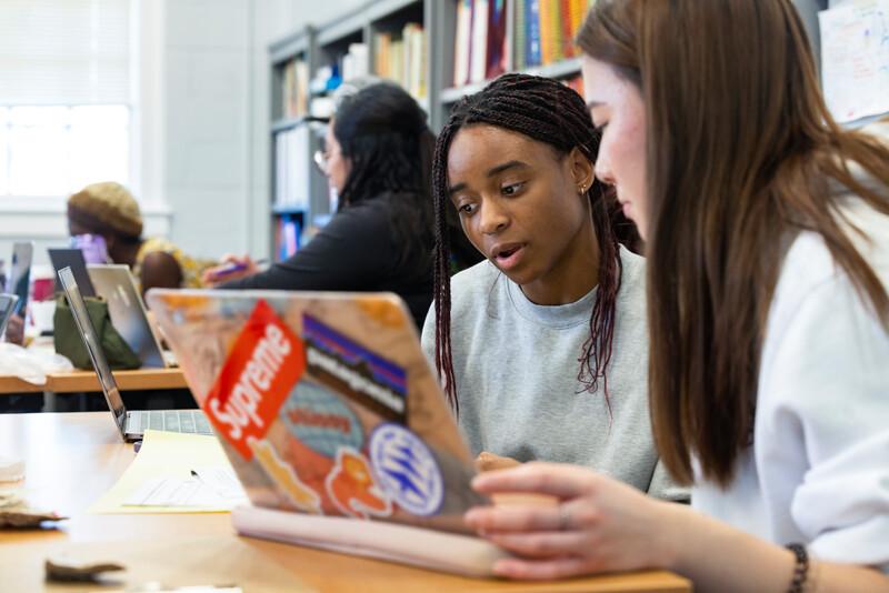 Two students in a classroom working on one laptop.