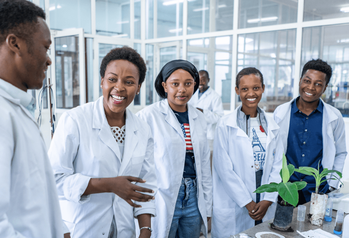 Students pose in a lab wearing white coats.