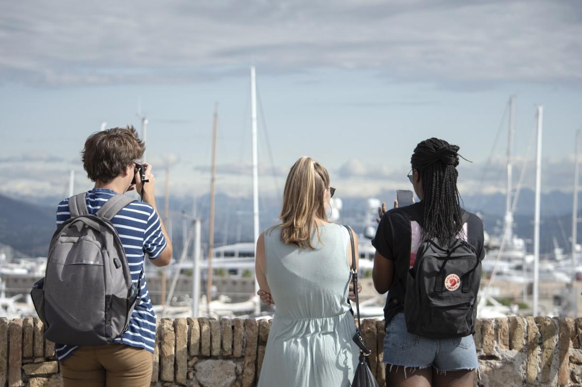 Three students facing a marina taking photos.