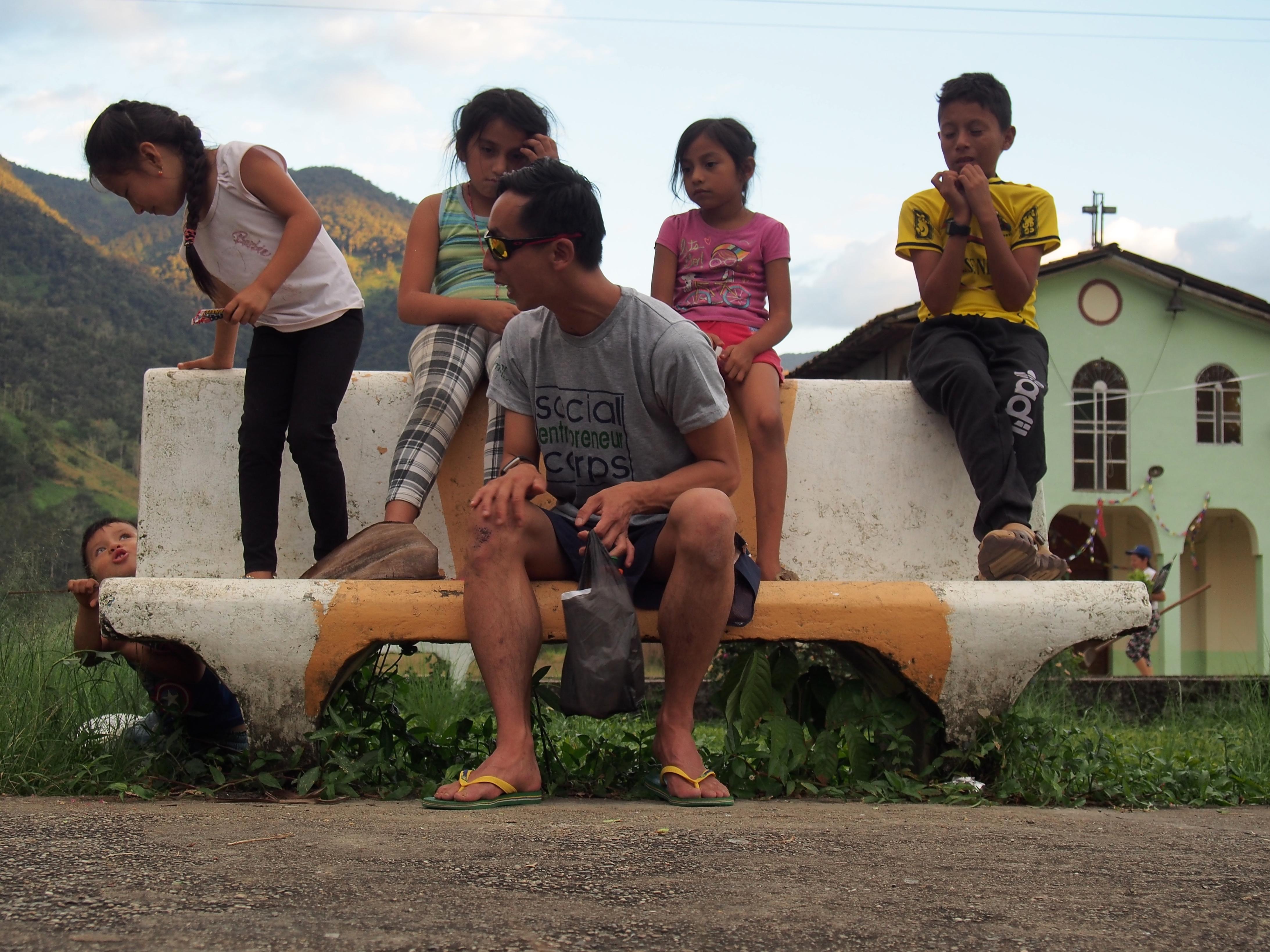 Man poses with children on a bench with a green house in the background.