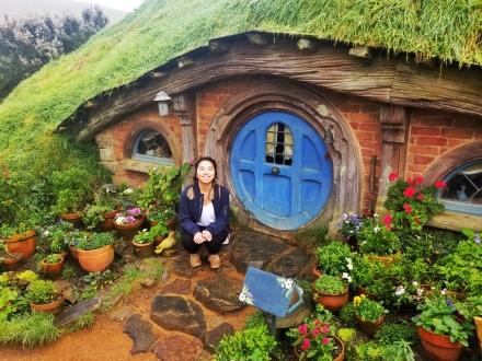 Ivy Li crouches in front of a hobbit home in New Zealand.
