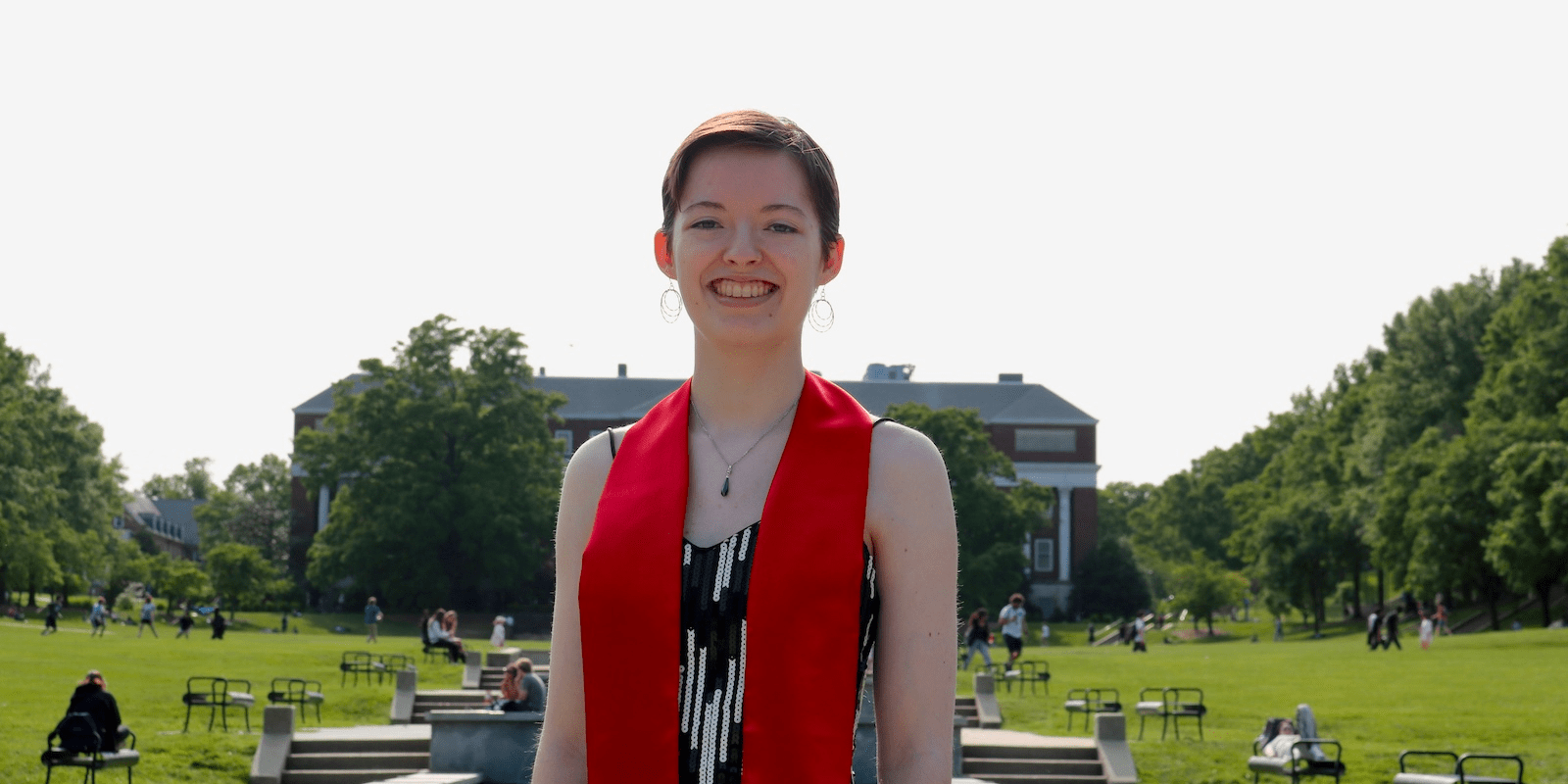 Paulina Leder '23 wearing red graduation stole standing on McKeldin mall