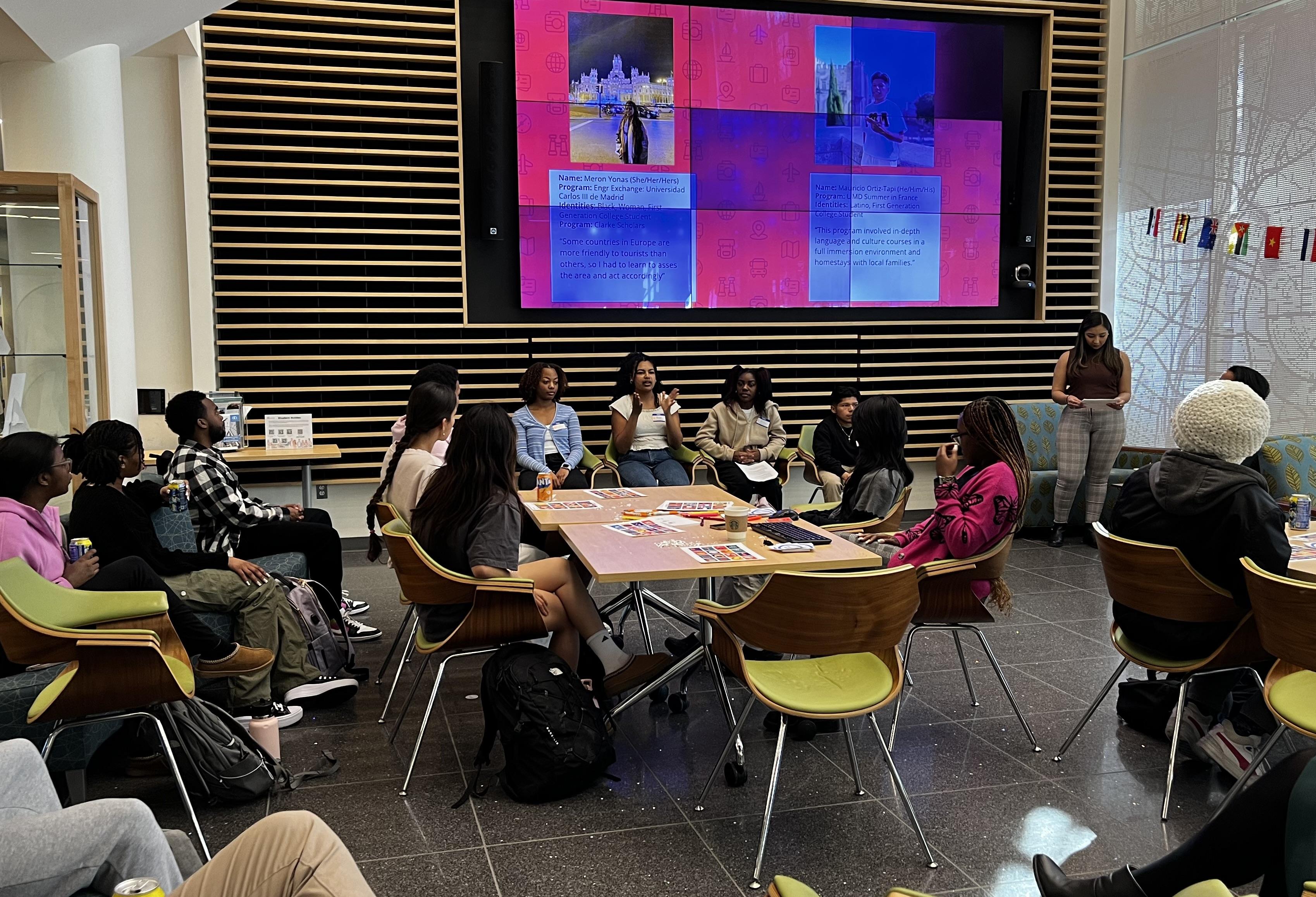 Attendees listen to the students of color panel in Global Crossroads in front of large screens