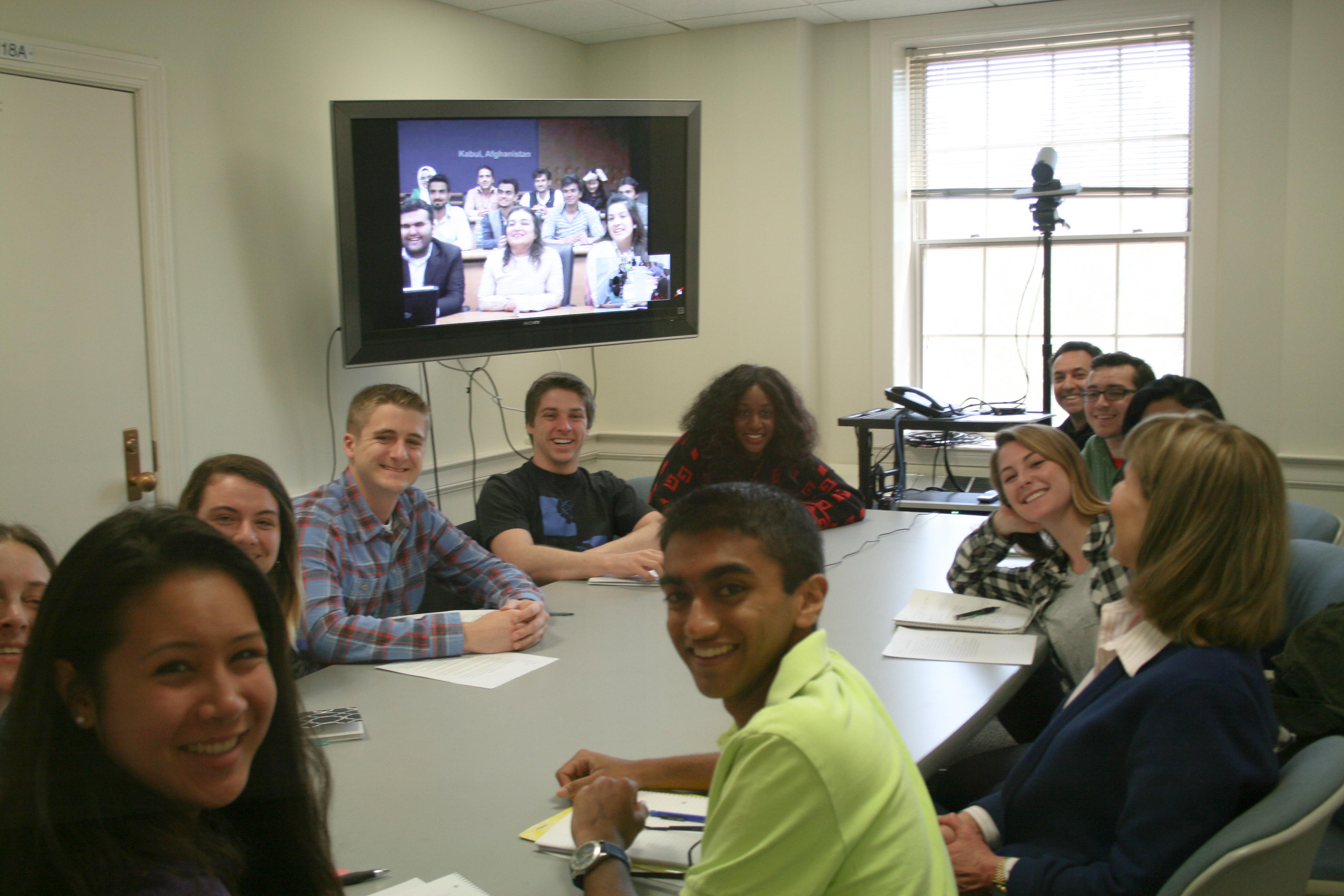 University of Maryland students sit around a table smiling, with American University of Afghanistan students on the television screen. 