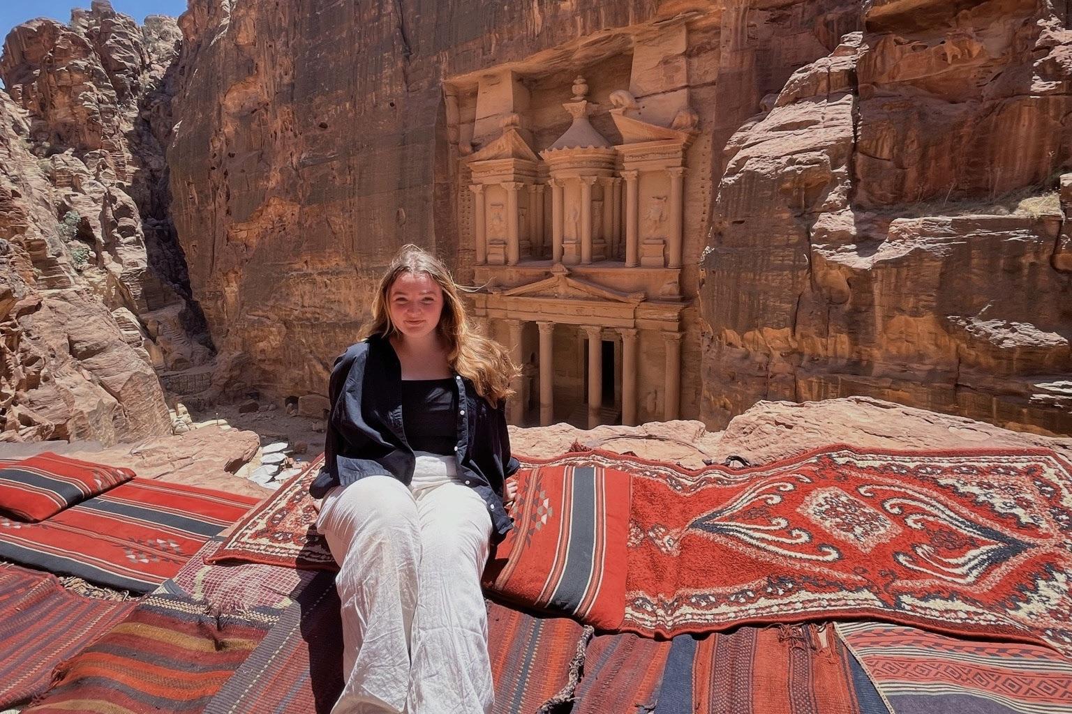Amaya Greenburg sits on Moroccan rugs on a cliff's edge in front of Petra