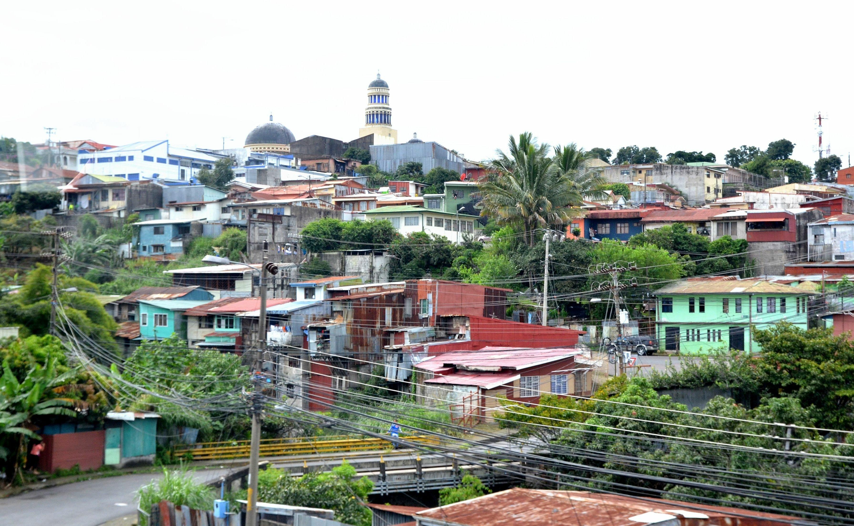 The city of San Jose, Costa Rica from an overlook. There is lush, green vegetation between brightly colored buildings.