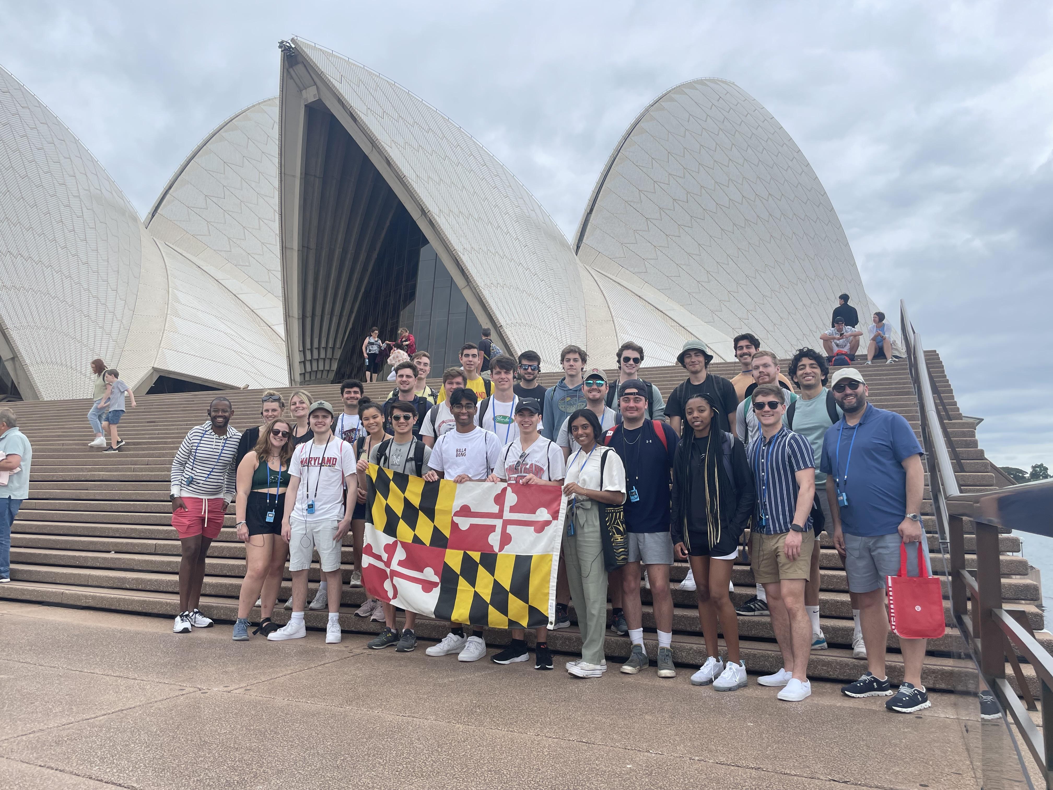 Group of UMD students in front of the Sydney Opera House holding a Maryland State flag.