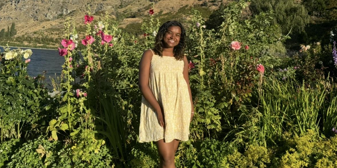 Ru stands in front of a garden wearing a yellow sundress.