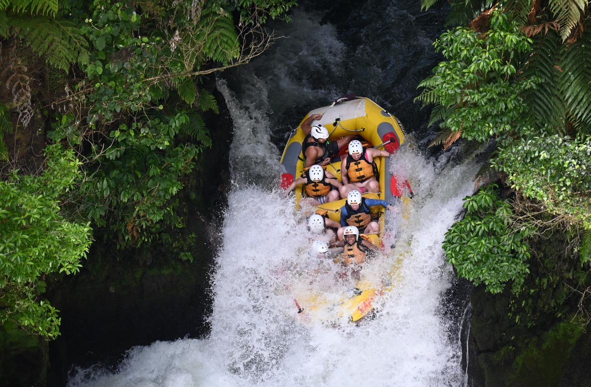 A group of people descend down a waterfall in a raft surrounded by lush green vegetation.