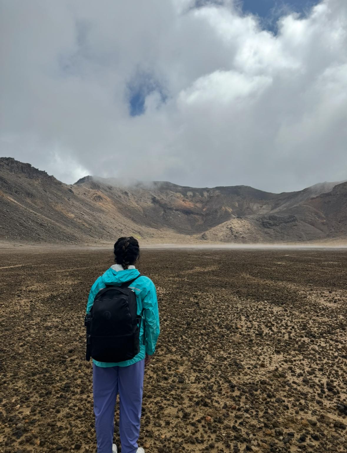 Ru stands in a valley observing the rugged landscape of the Tongariro Alpine Crossing, including rocky terrain and mountains in the background.