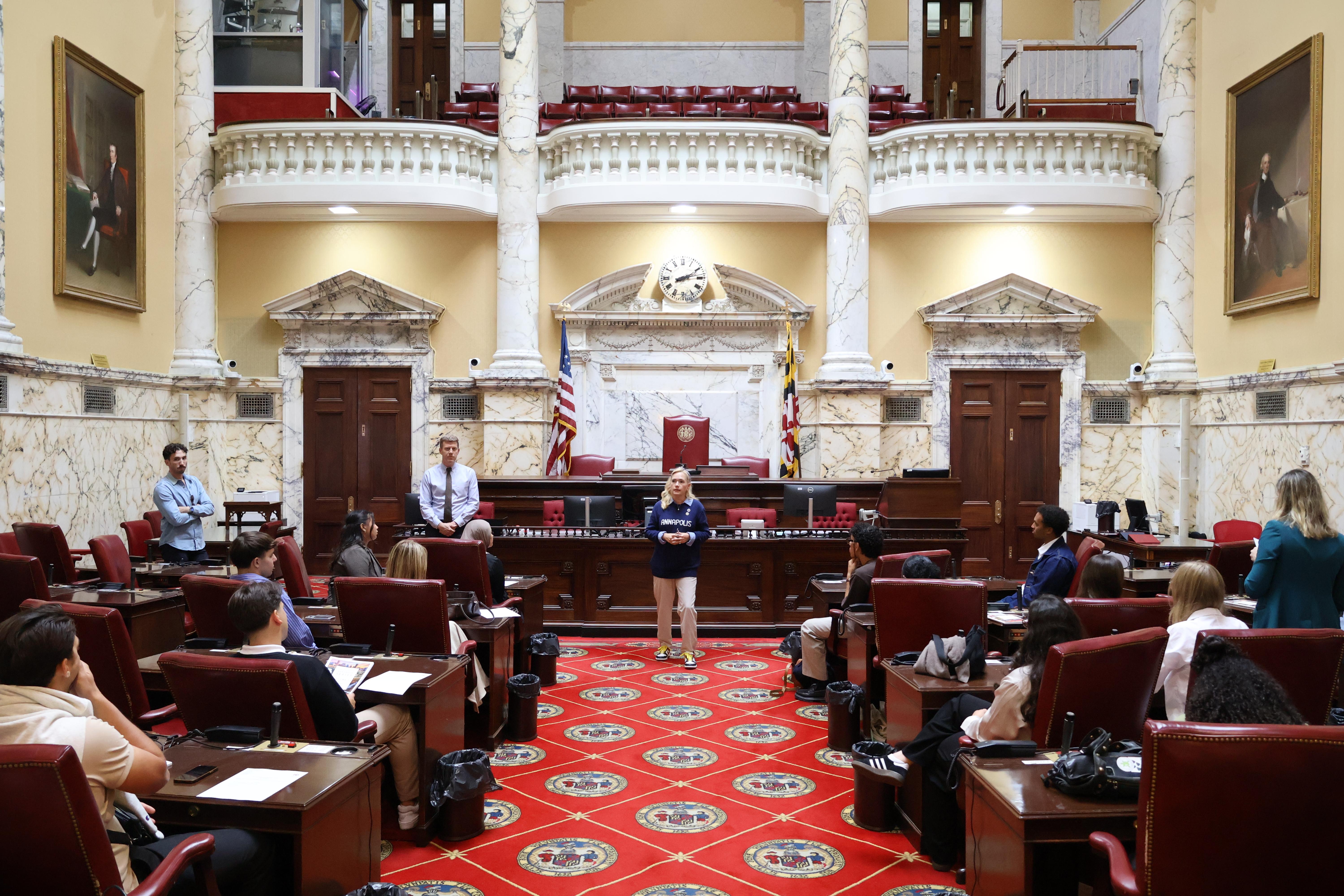 Woman stands in the center aisle of the Maryland State House chamber